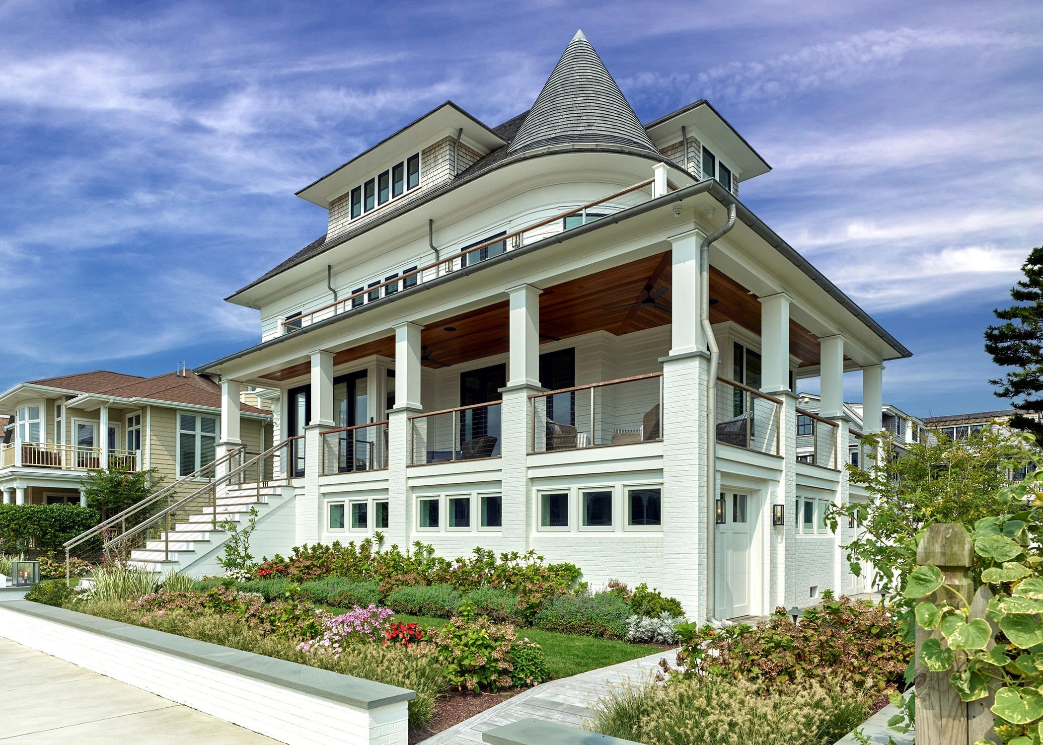 Modern coastal home with conical turret, white clapboard siding, columned front porch, and tiered decking.