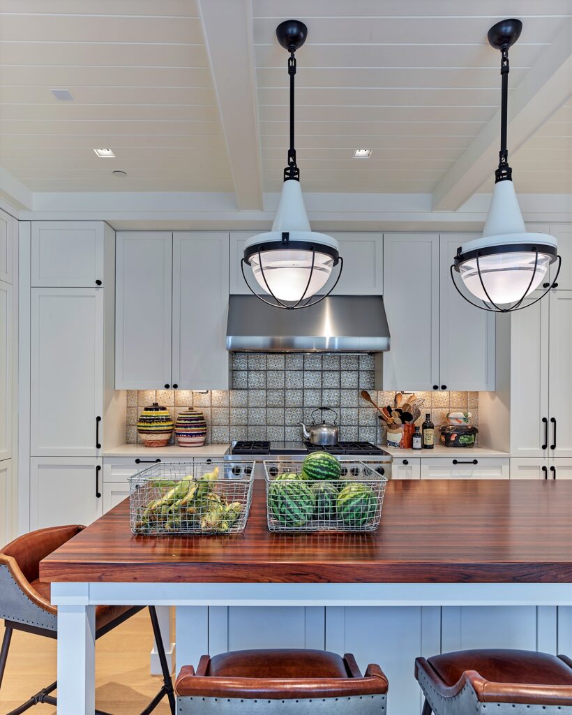 Modern kitchen with white shaker cabinetry, wood waterfall island countertop, stainless steel hood, patterned tile backsplash, and pendant lighting.