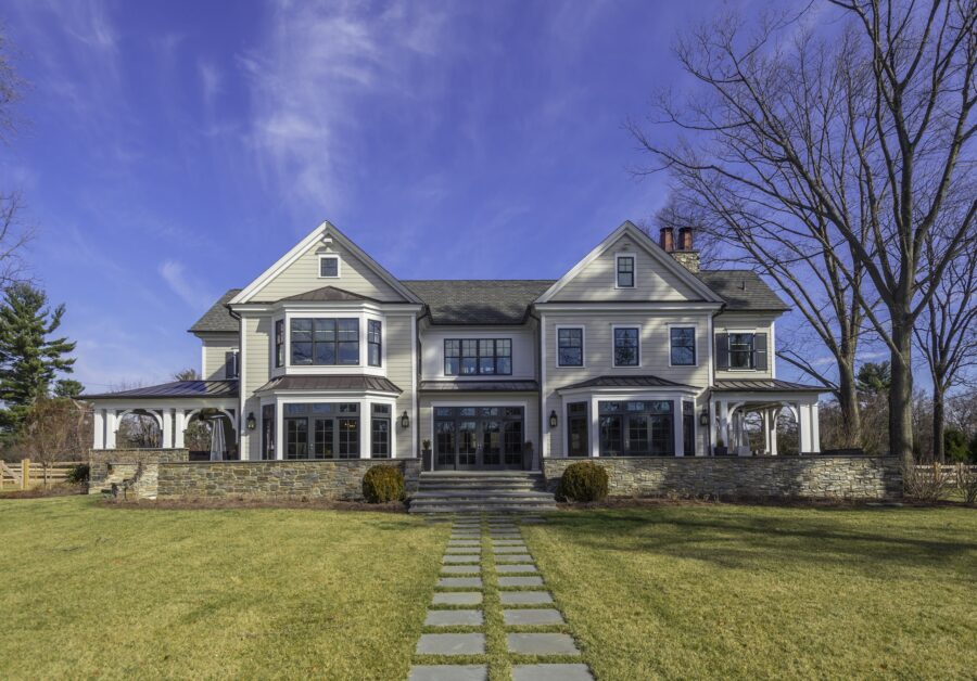 Modern farmhouse residence with white board-and-batten siding, stone base, gabled rooflines, and extensive glazing across front elevation.