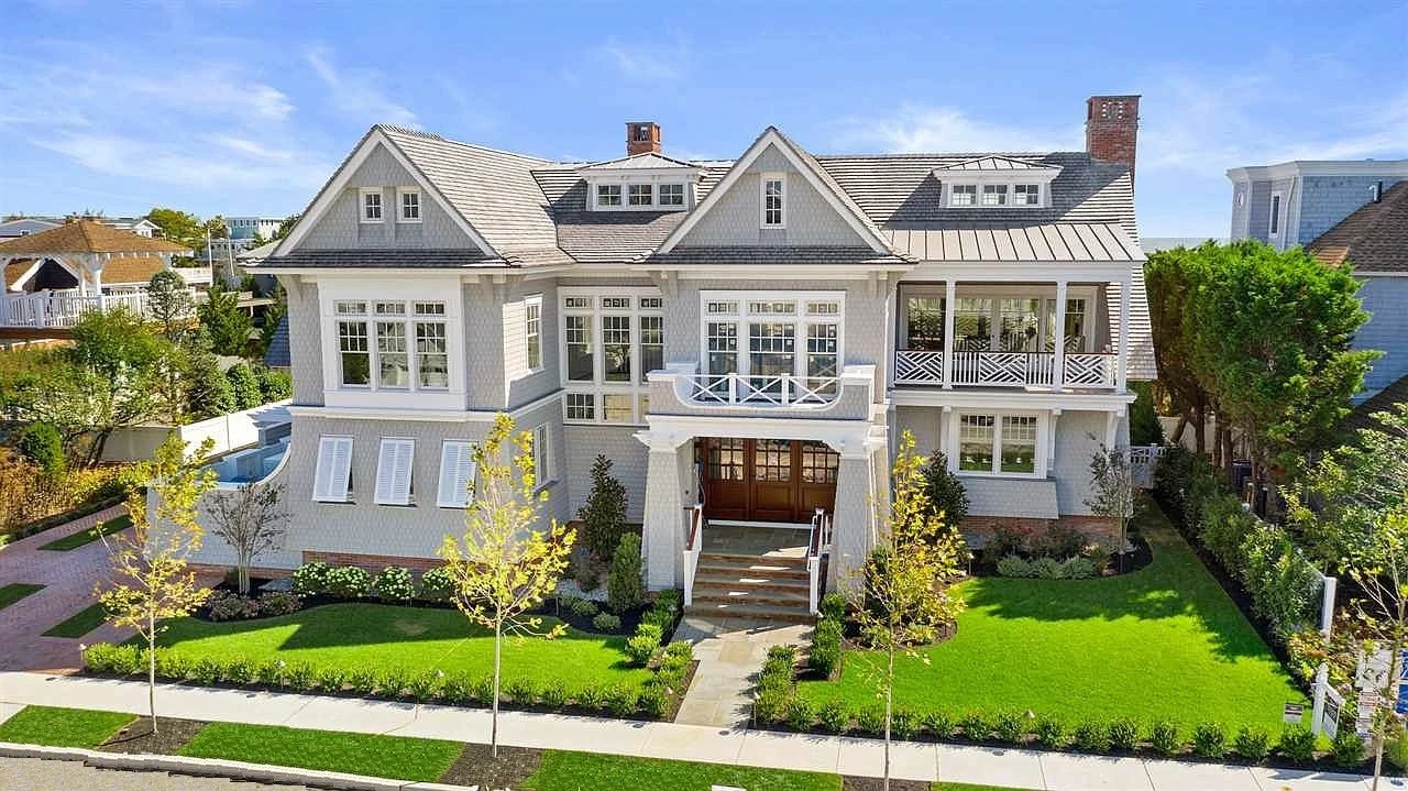 Modern farmhouse with gray shingle siding, multi-gable roof, and prominent covered front porch with cross-braced railings.