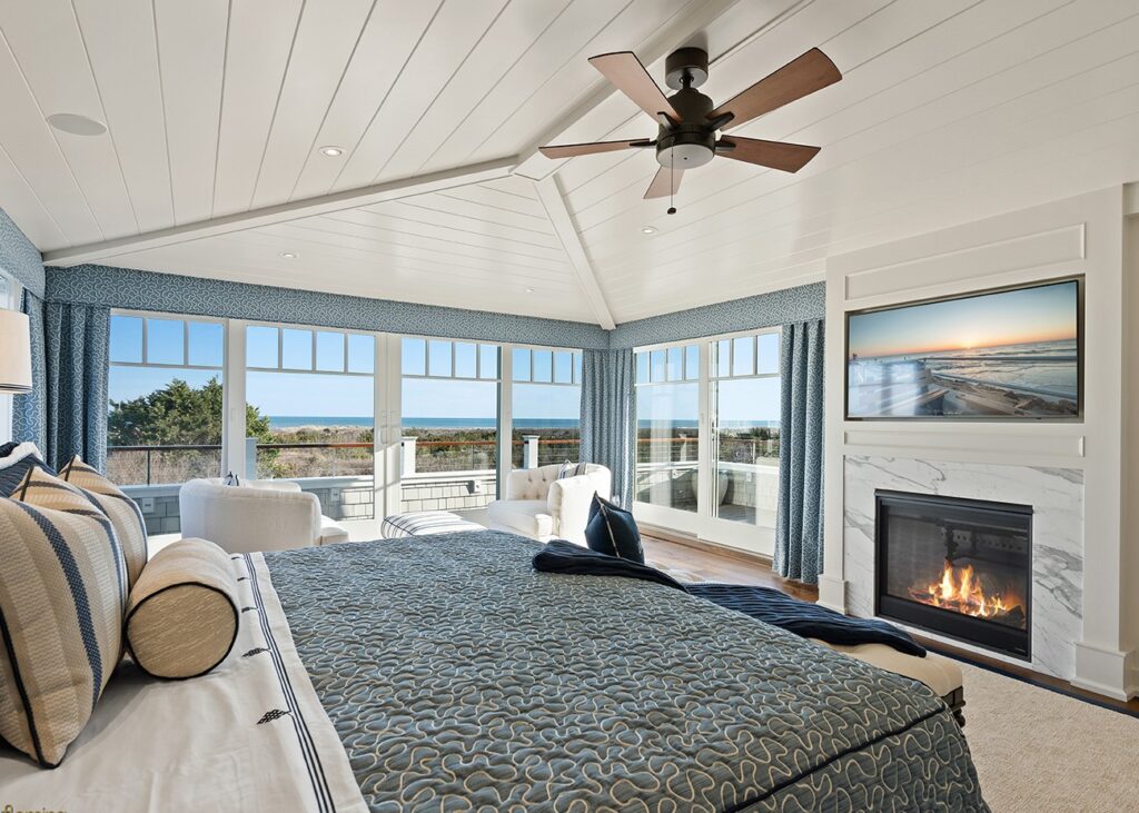 Modern coastal master bedroom with shiplap ceiling, glass doors, fireplace, and ocean views.