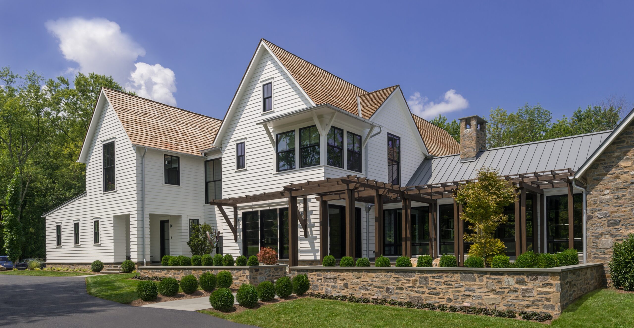 Modern farmhouse with white horizontal siding, stone accents, gabled rooflines, and timber pergola over rear terrace.