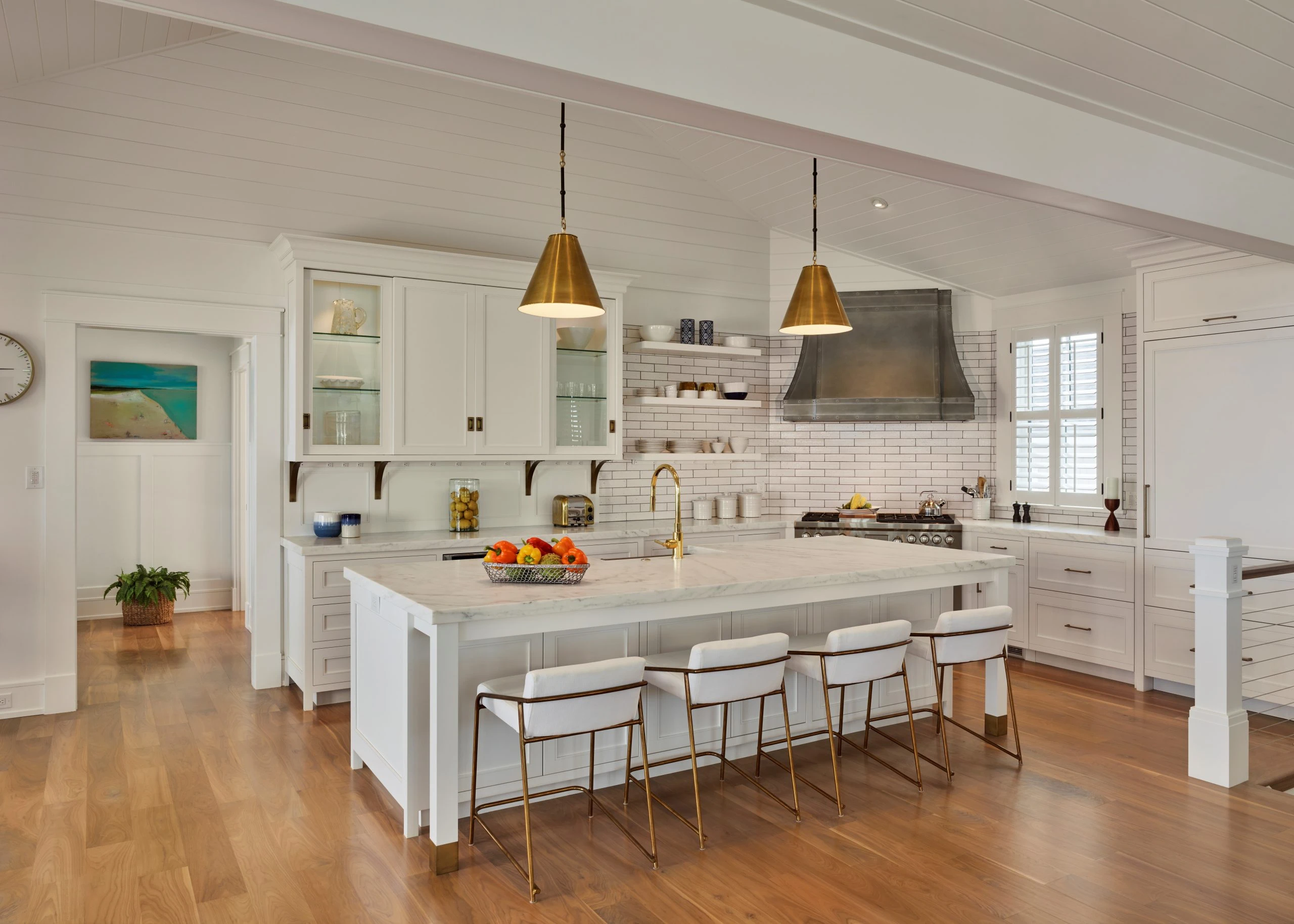 Modern kitchen with white cabinetry, marble countertops, subway tile backsplash, brass pendant lights, and waterfall island.