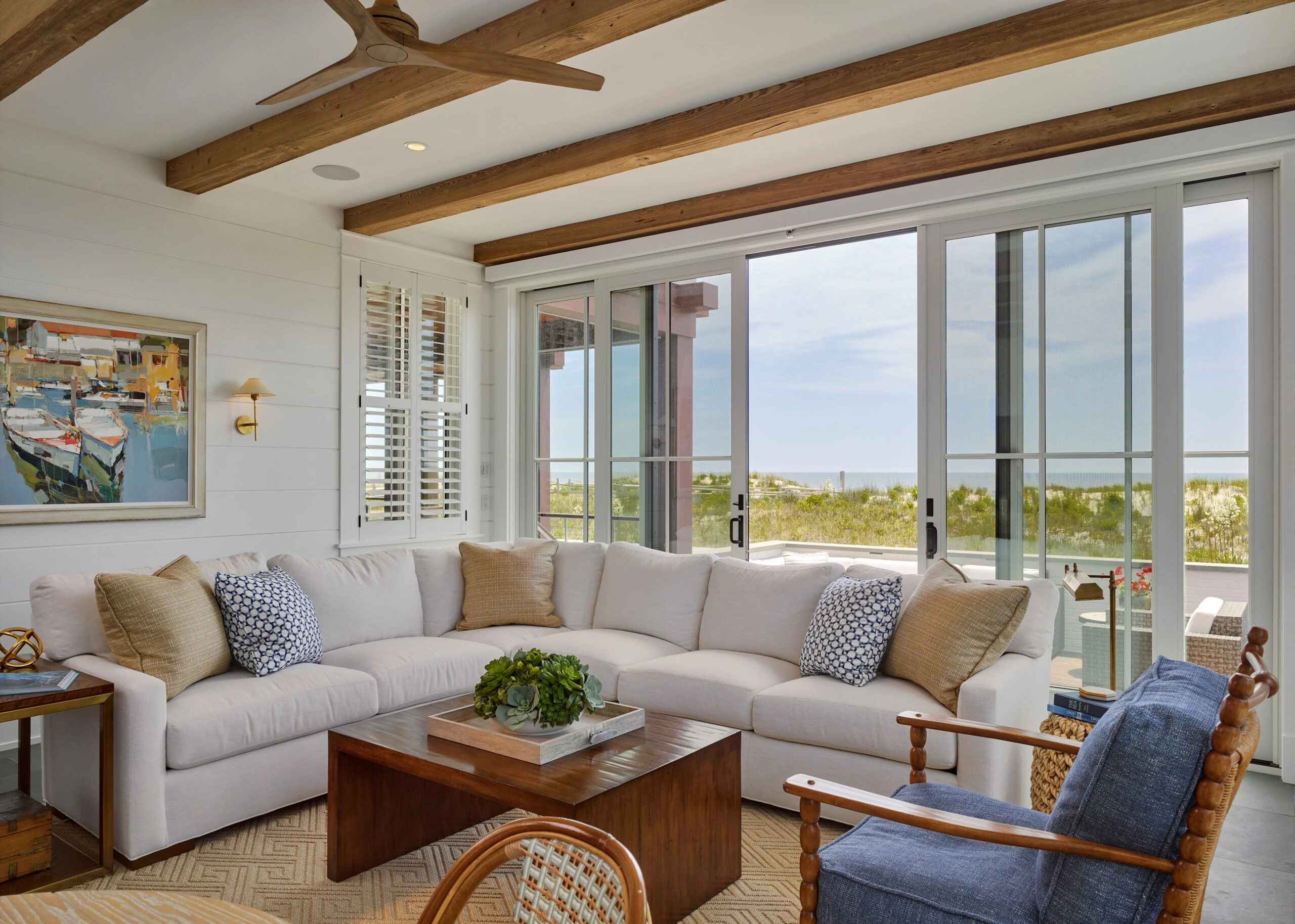 Modern coastal living room with exposed wood beams, floor-to-ceiling glazed doors, and ocean views.