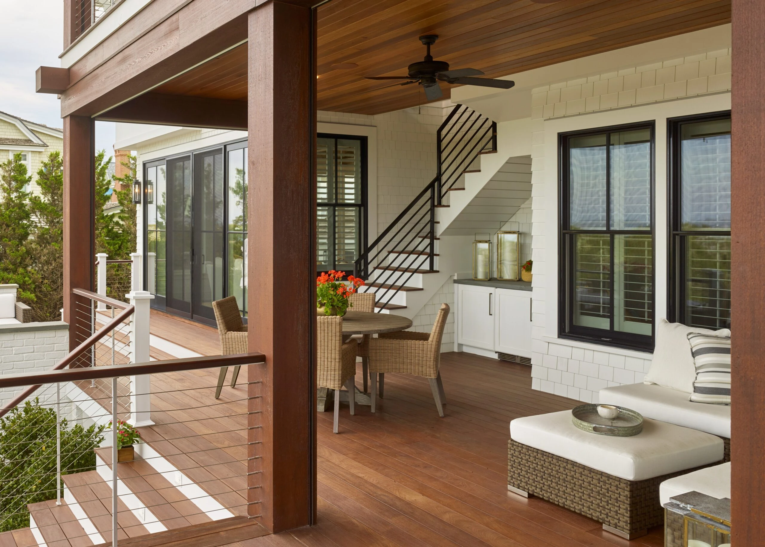Modern covered porch with wood ceiling, metal railing, and interior staircase visible through glass doors.
