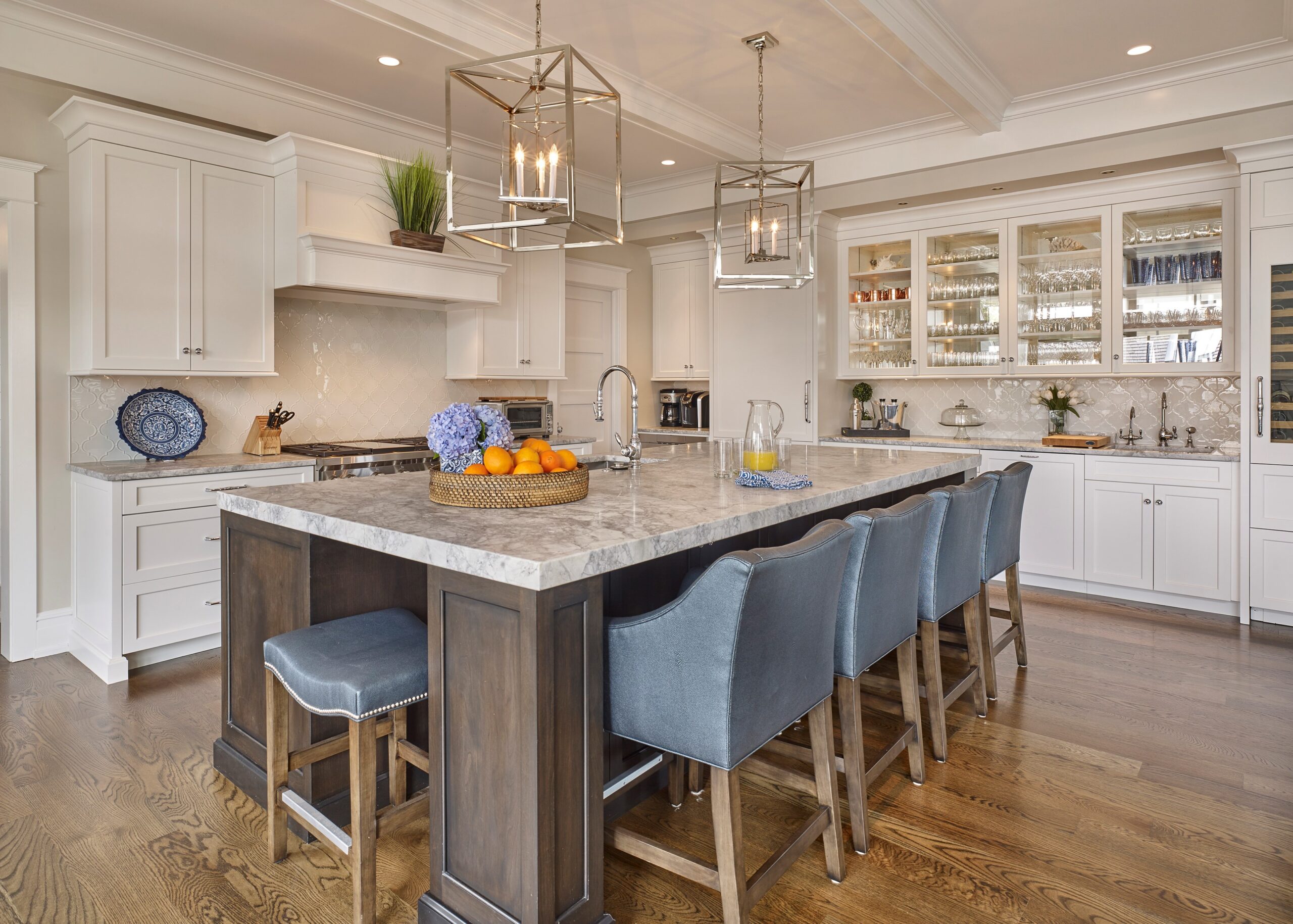 Luxury kitchen with white cabinetry, marble island, coffered ceiling, and glass-fronted upper cabinets.