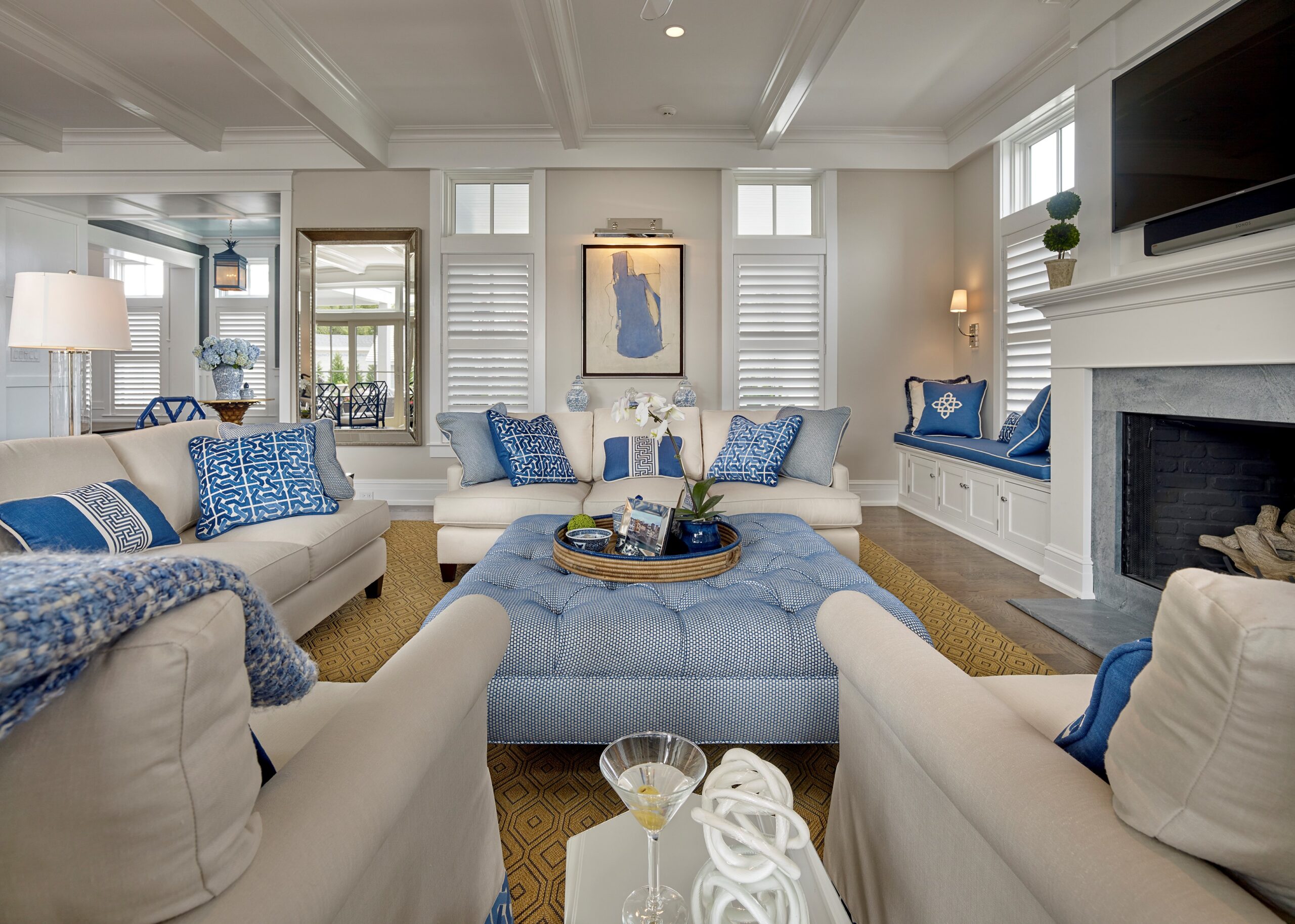 Coastal-style living room with coffered ceiling, built-in cabinetry, fireplace with marble surround, and blue-and-white color scheme.