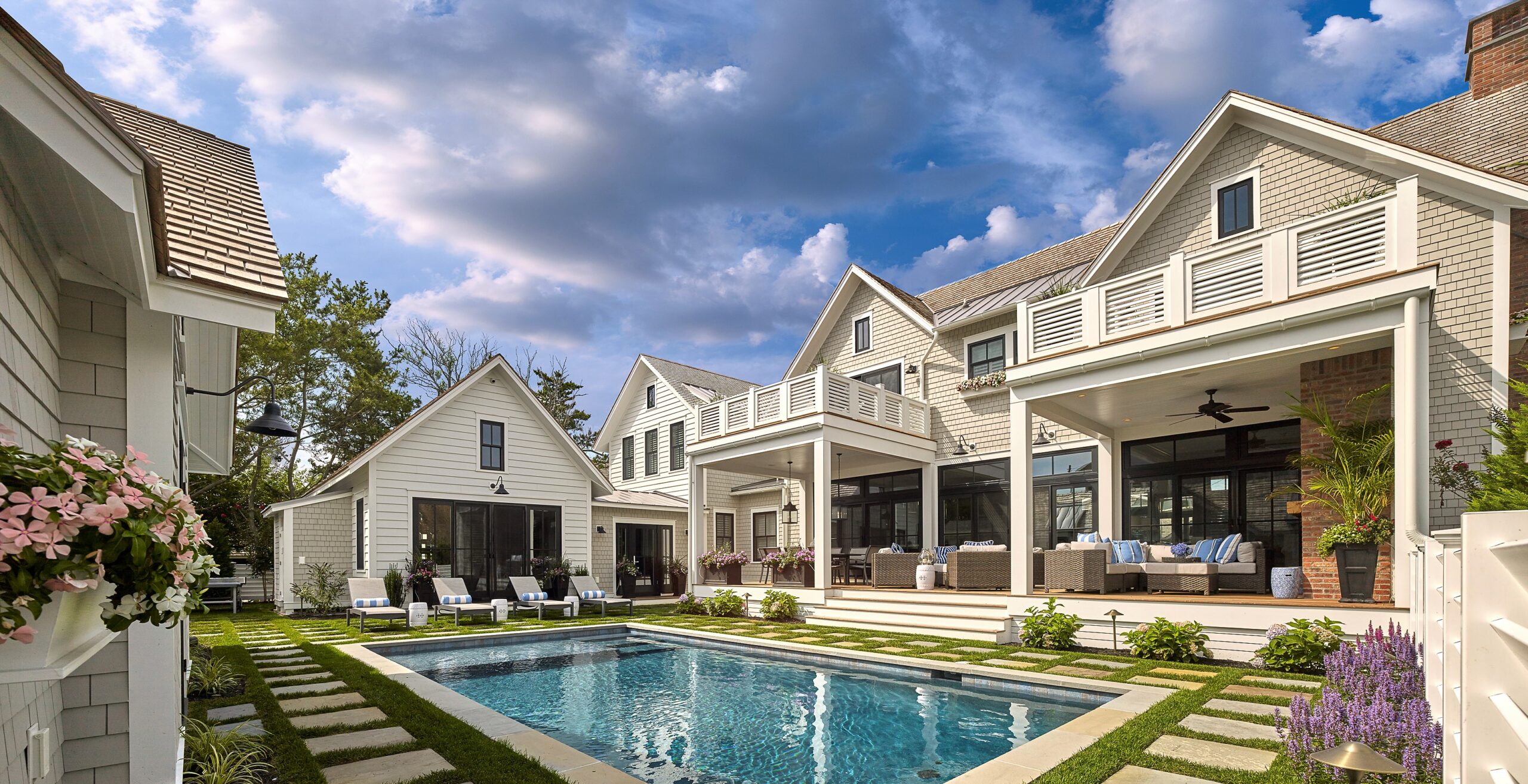 Modern residential estate featuring clean-lined white clapboard facades, expansive glass doors, and covered porches overlooking a rectangular swimming pool with stepping stone deck.