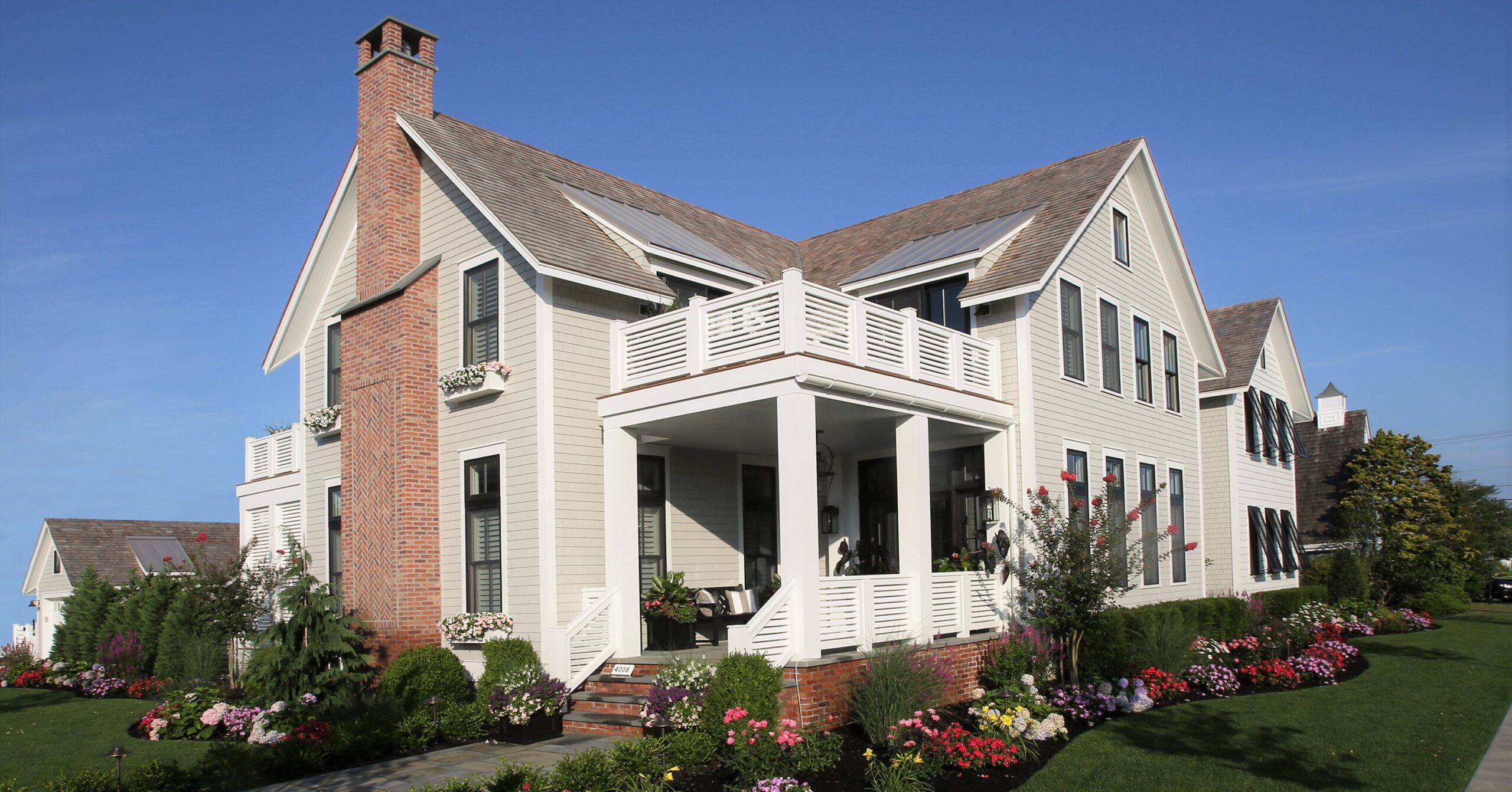 Modern farmhouse with white siding, brick chimney, dual gables, and wraparound porch with columns.