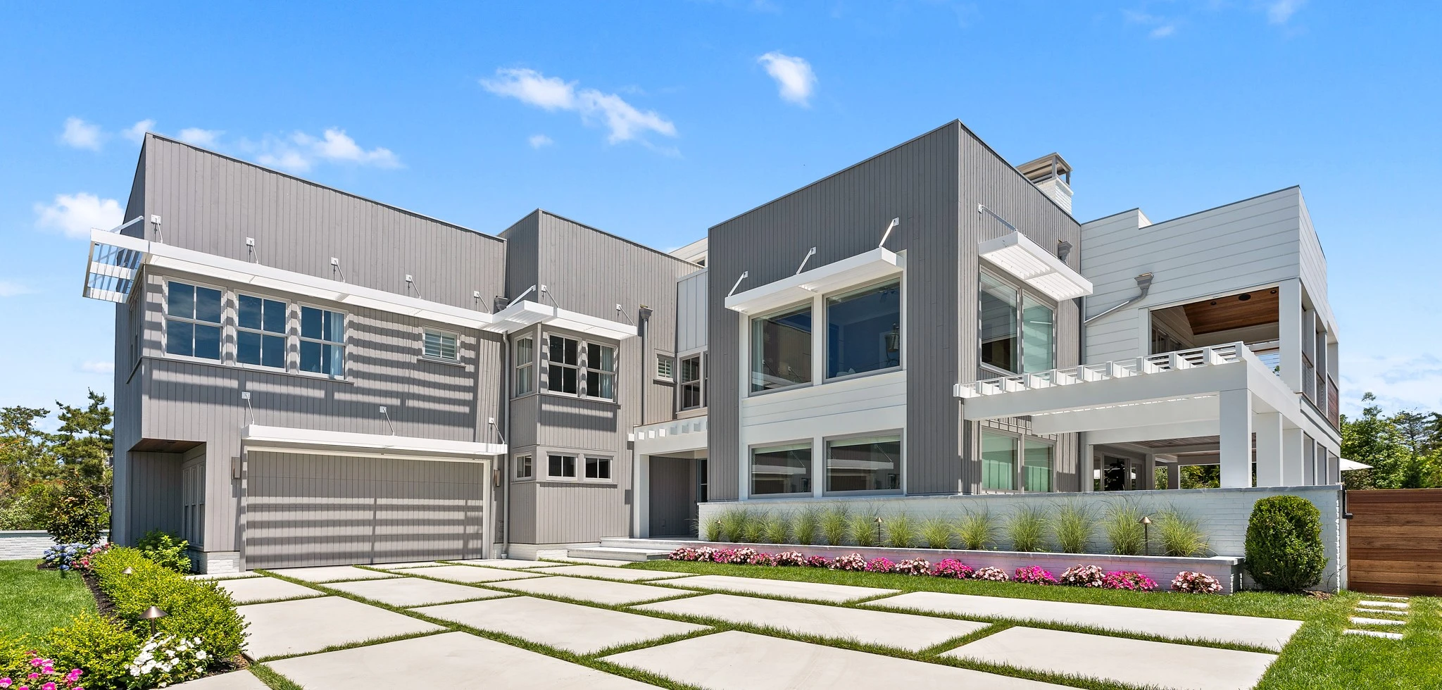 Modern two-story residential home with mixed metal and white panel facade, horizontal striping, large windows, and geometric concrete driveway.