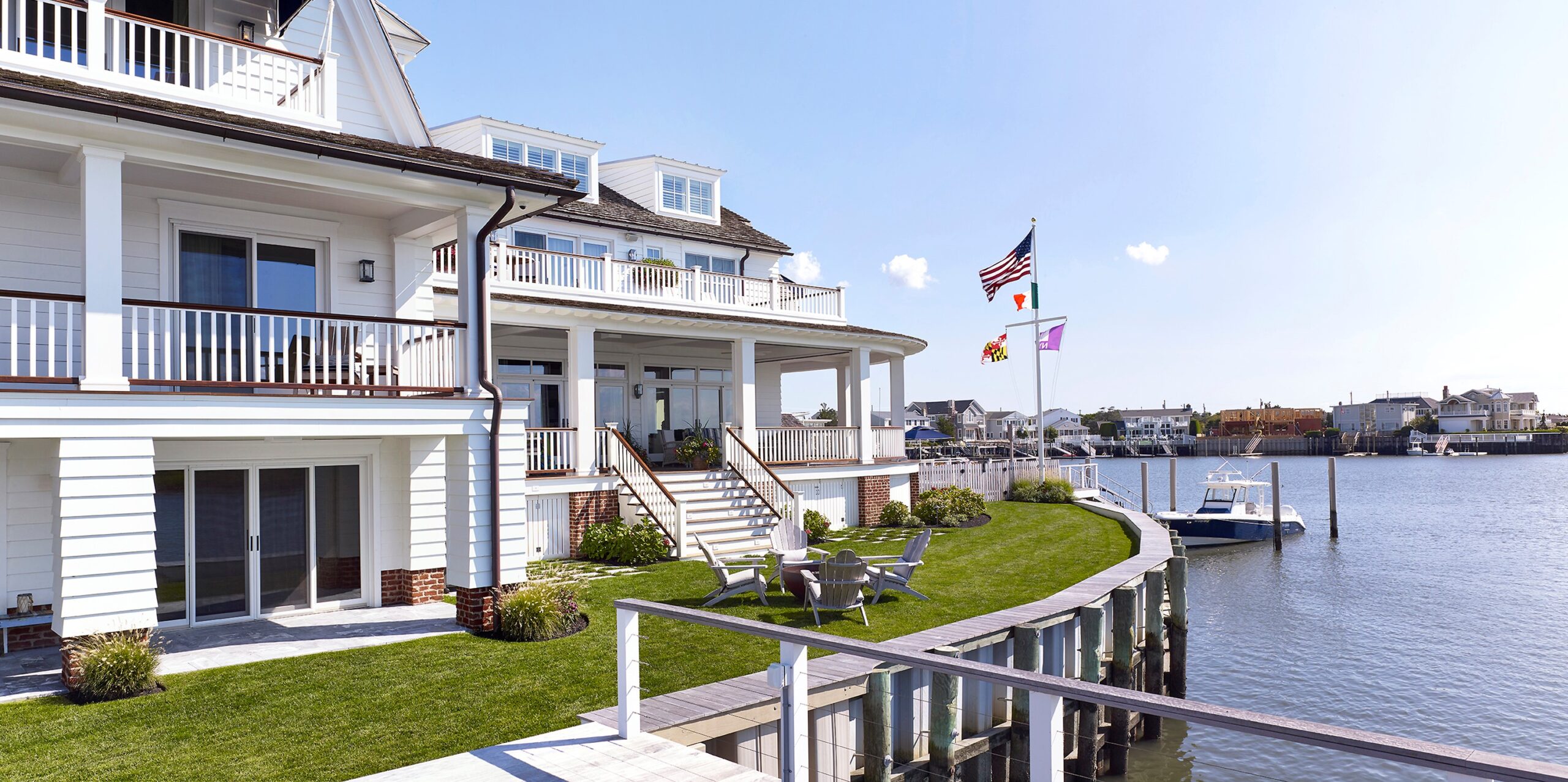 Waterfront colonial revival residence with white clapboard siding, widow's walk, and covered portico overlooking private dock.