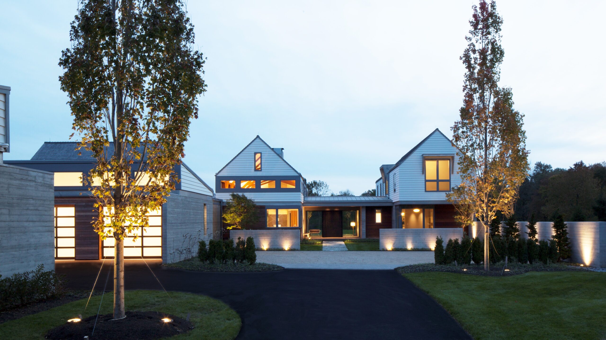 Modern farmhouse with board-and-batten siding, gabled rooflines, clerestory windows, and integrated landscape lighting at dusk.