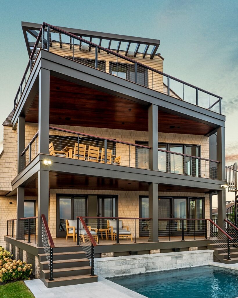 Modern three-story residential home with cedar shingle facade, steel frame, glass railings, and cantilevered decks overlooking a pool.