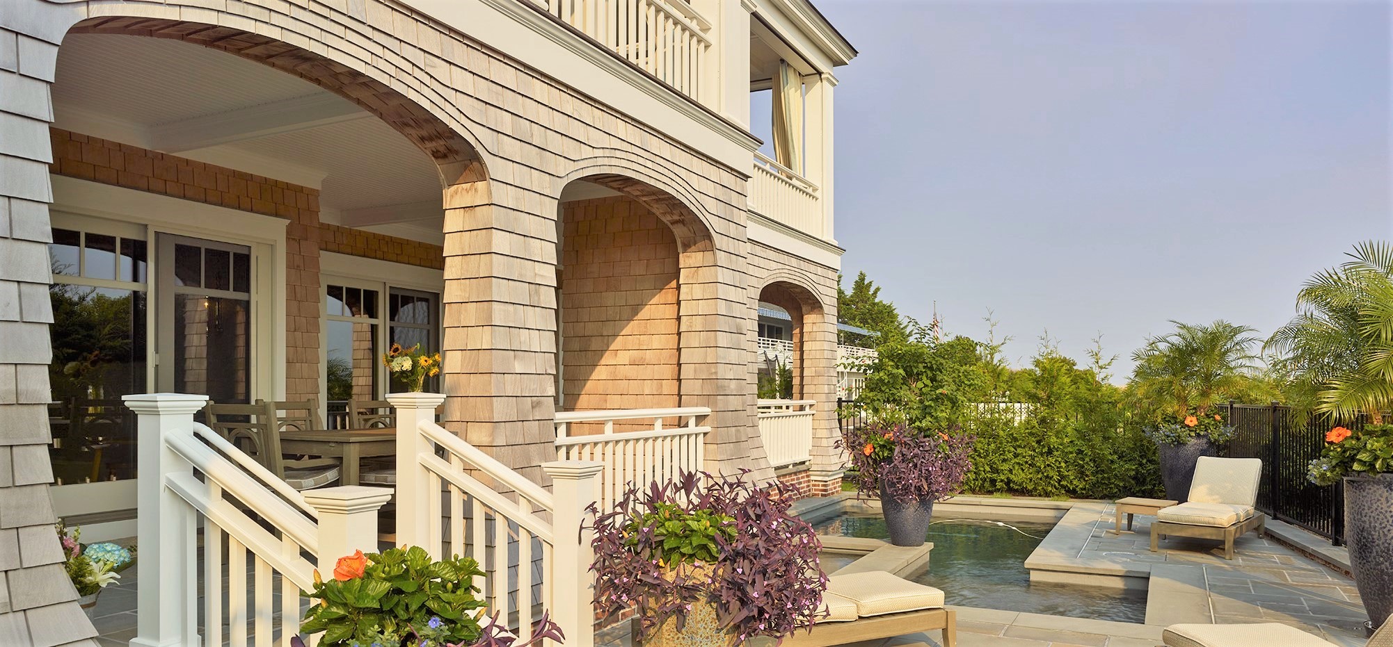Residential facade with arched openings, cedar shingle siding, white railings, and adjoining rooftop terrace with stone paving.