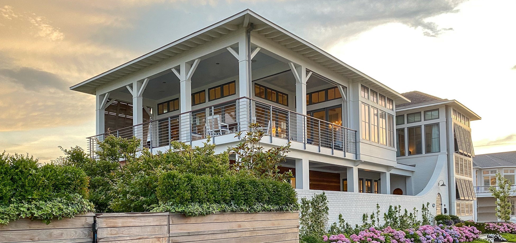 Modern coastal home with white exterior, multi-level design, horizontal cable railings, and expansive windows with natural wood frames.