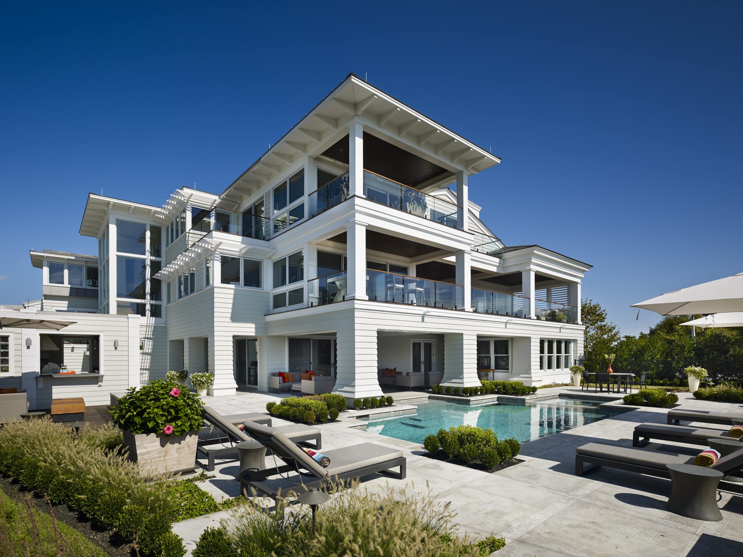 Modern three-story white residential home with horizontal siding, extensive glazing, and cantilever overhangs overlooking a swimming pool.
