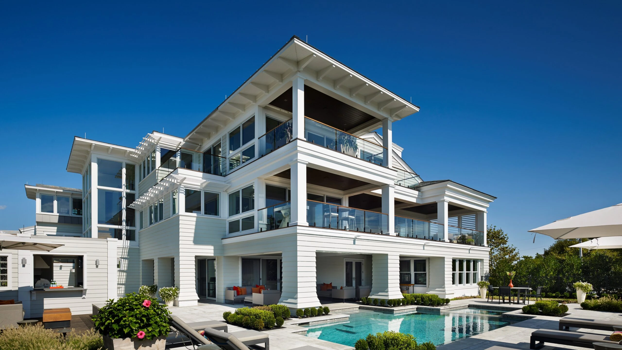 Modern three-story coastal residence with white horizontal siding, extensive glazing, cantilevered overhangs, and swimming pool.