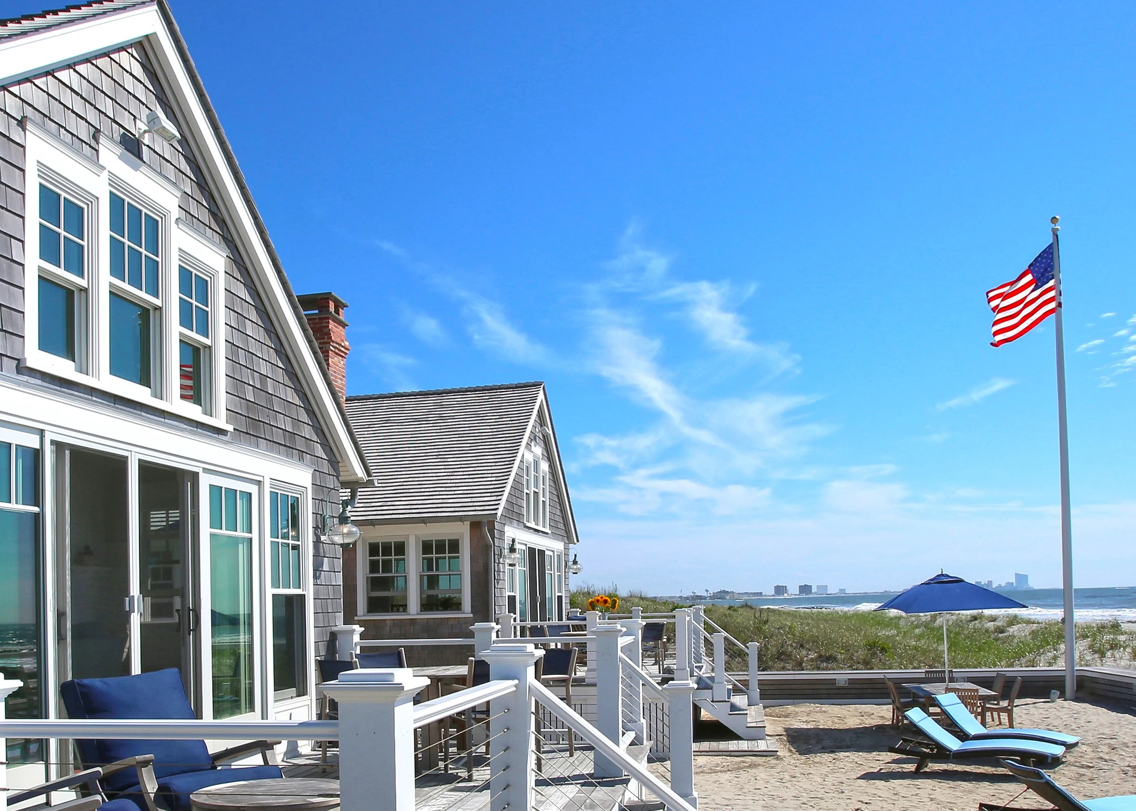 Modern coastal residence with shingle siding, multi-pane windows, and elevated deck overlooking beach and waterfront.