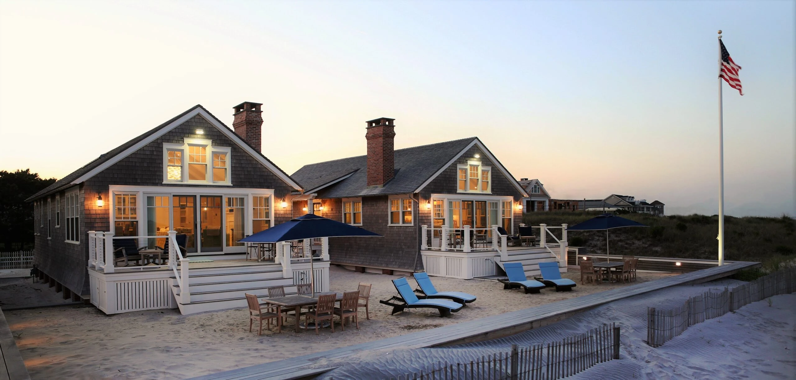 Contemporary beachfront residence with dual gabled sections, white trim detailing, and expansive glazing overlooking sandy dunes.