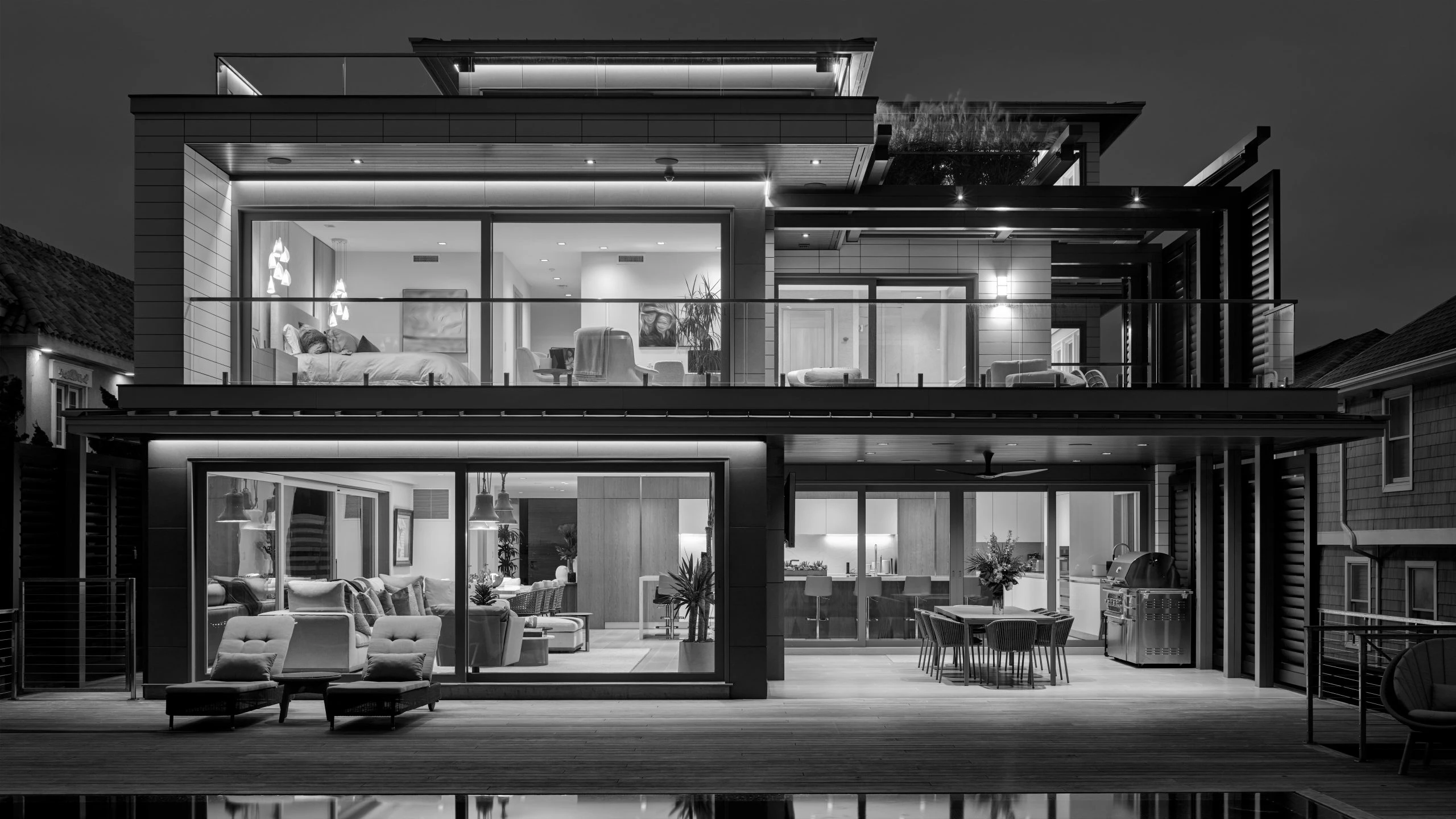 Modern two-story residence with extensive glazing, black aluminum framing, cantilevered upper level, and integrated outdoor living spaces.