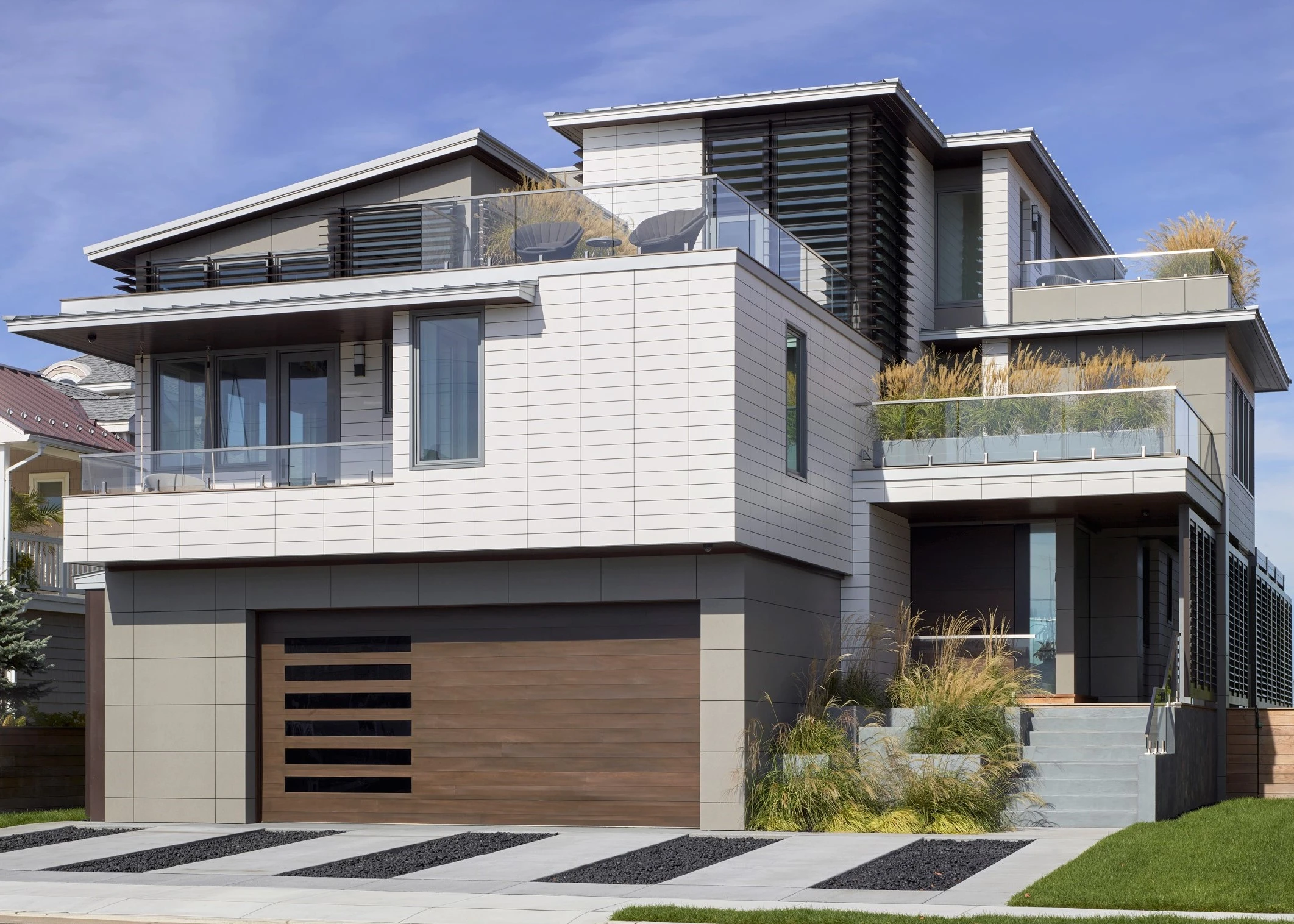Modern two-story residence with horizontal wood and composite cladding, cantilevered balconies, and integrated garage featuring horizontal slat detailing.