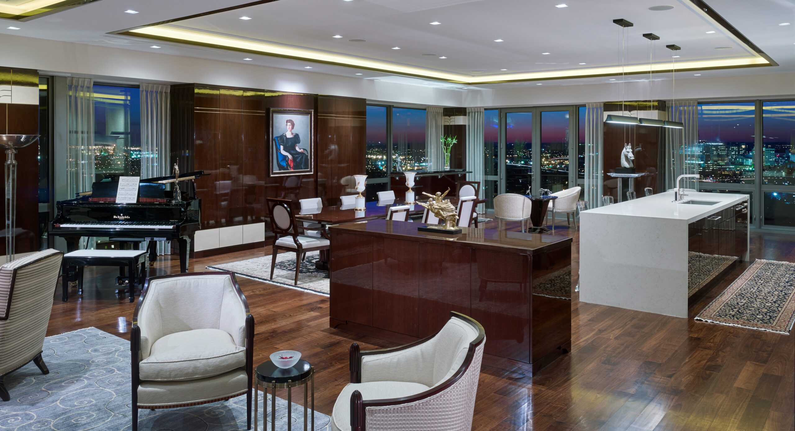 Luxury penthouse living room with dark wood millwork, piano, curved desk, cream seating, and floor-to-ceiling windows overlooking city skyline at dusk.