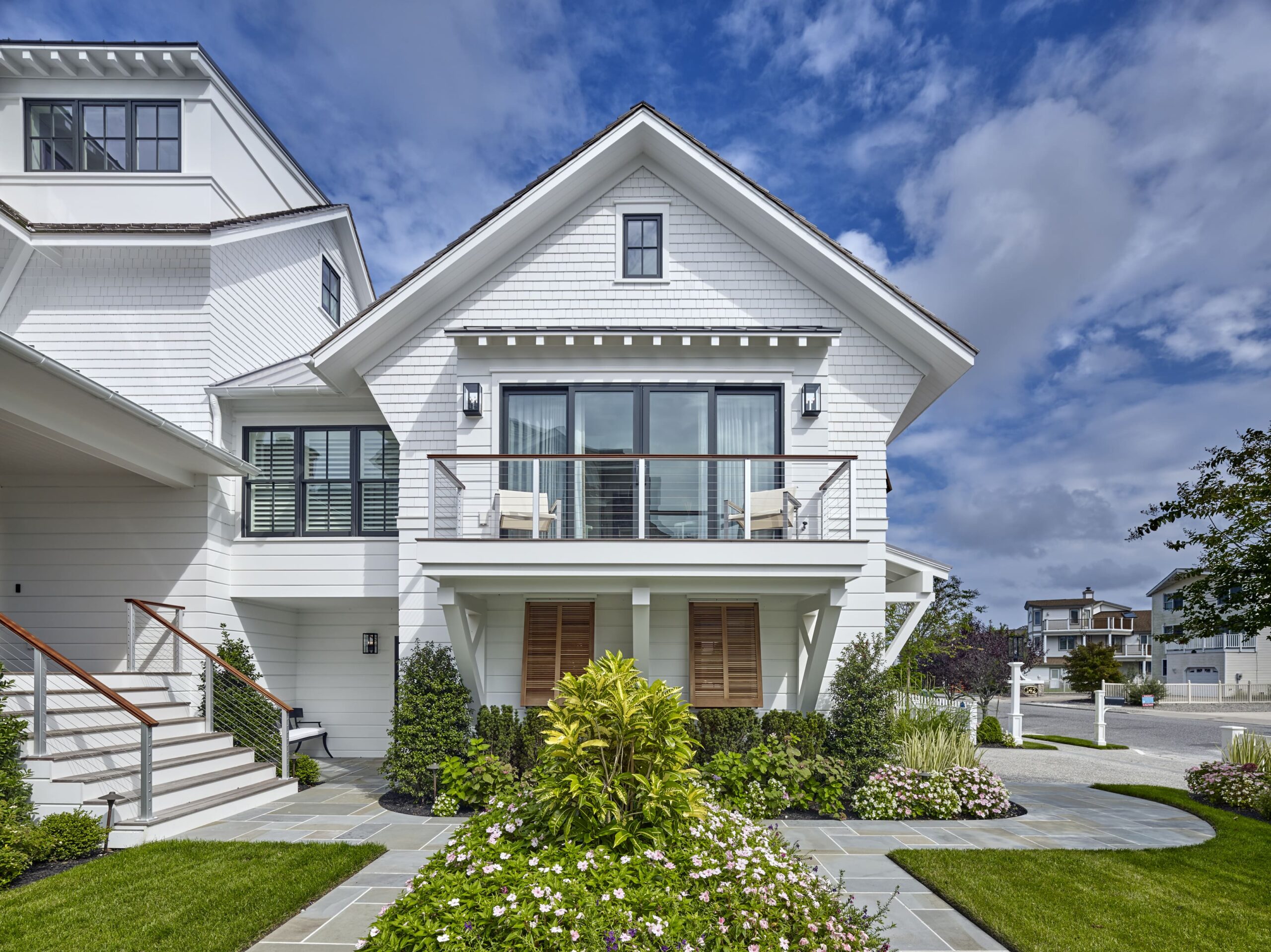 Modern farmhouse with white shingle facade, multi-level design, and horizontal railing balcony overlooking manicured landscape.