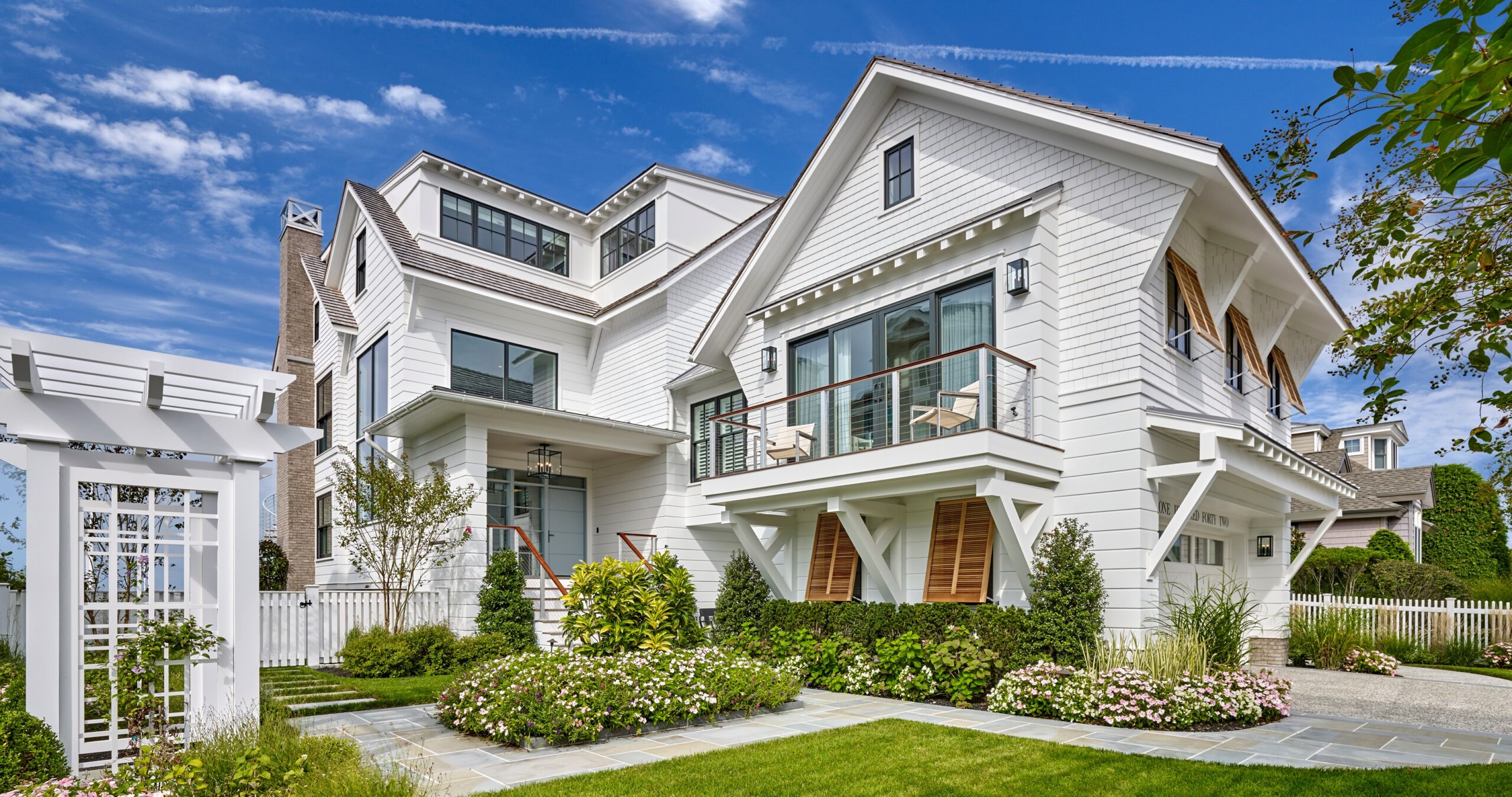 Modern farmhouse with white board-and-batten siding, multiple gables, and X-braced exterior shutters.