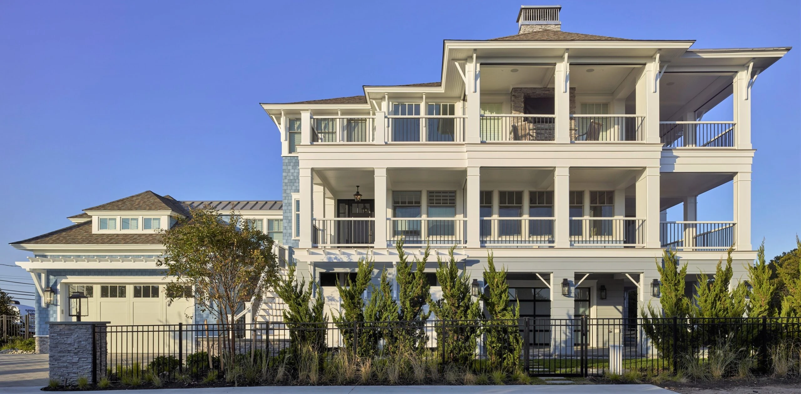 Modern coastal residence featuring columned facade, multi-level design with extensive porches, and mixed stone and board-and-batten cladding.