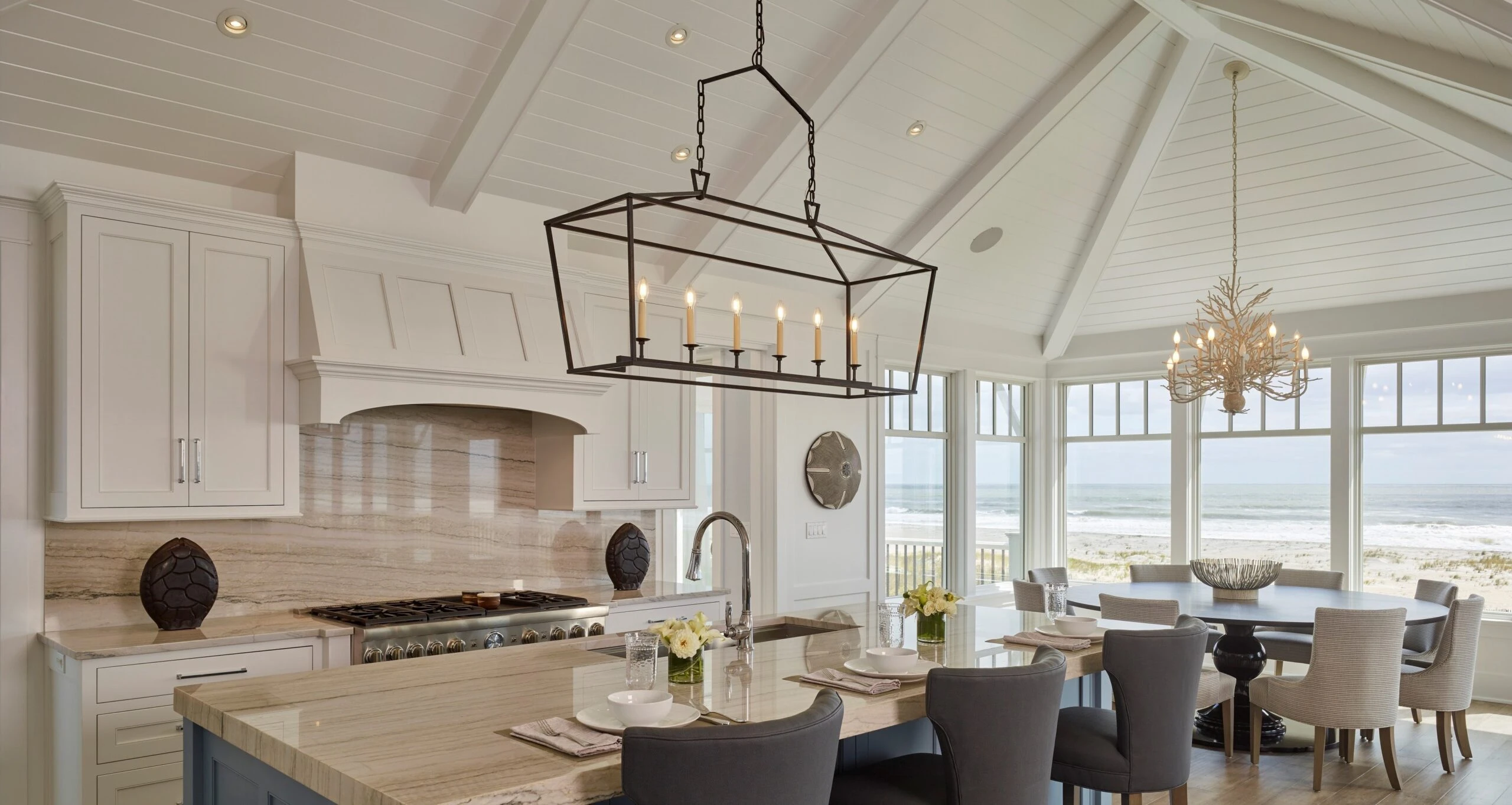 Coastal kitchen and dining area with white cabinetry, wood countertops, coffered ceiling, and expansive windows overlooking beach views.