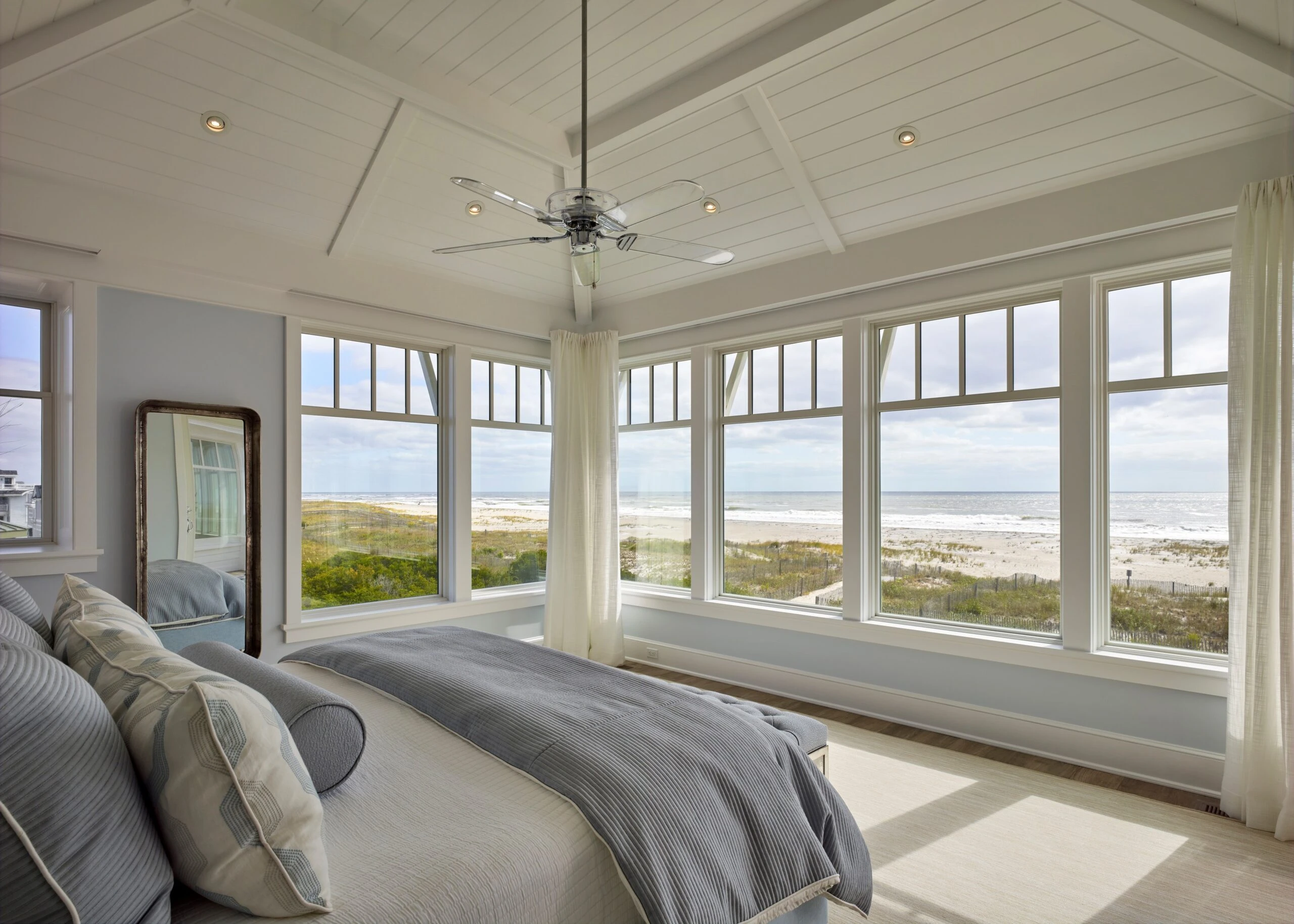 # Bedroom with expansive coastal views framed by clerestory windows, white coffered ceiling, and cream curtains.