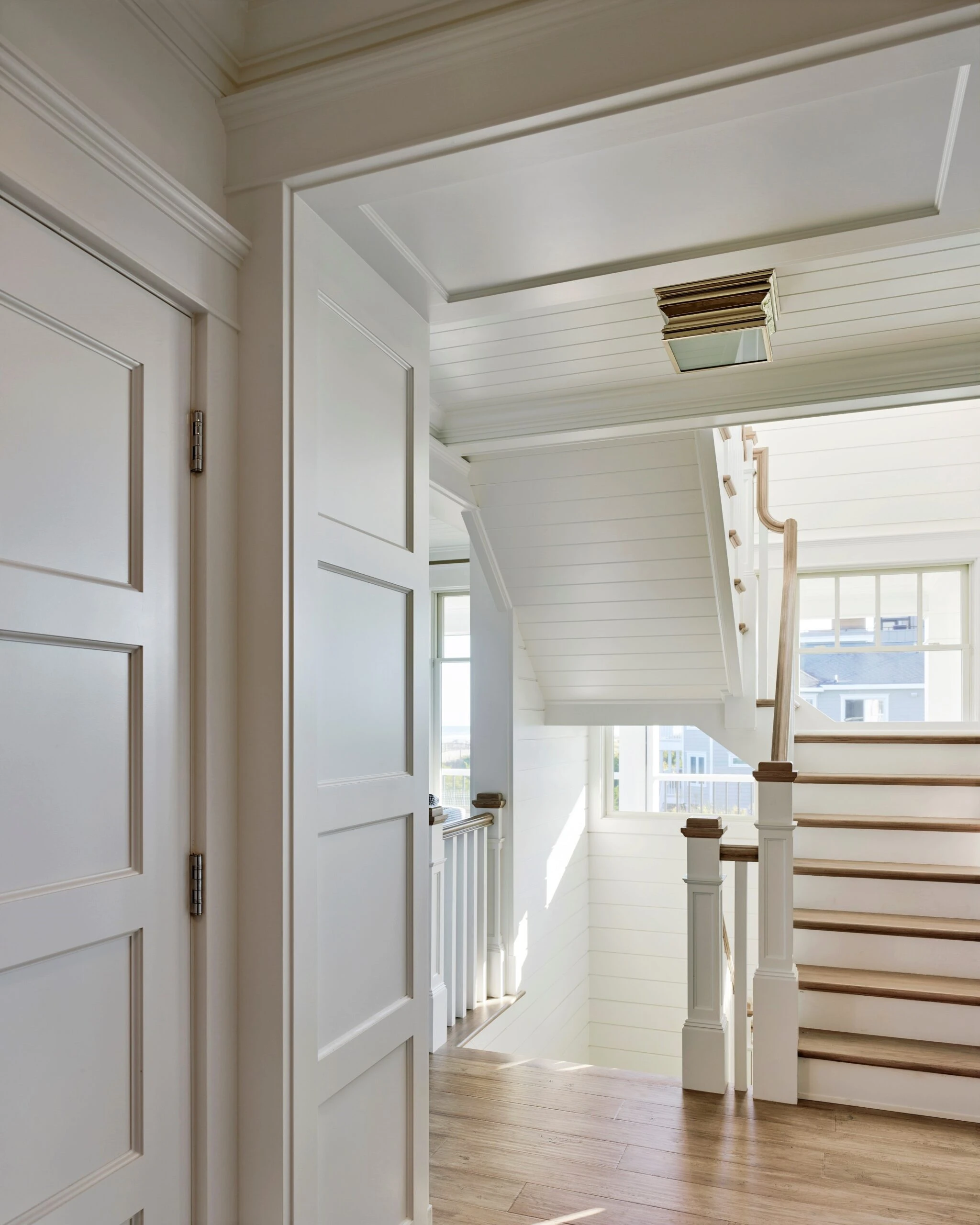 Bright residential hallway with shiplap walls, coffered ceiling, hardwood floors, white paneled doors, and staircase with wood treads and white balusters.
