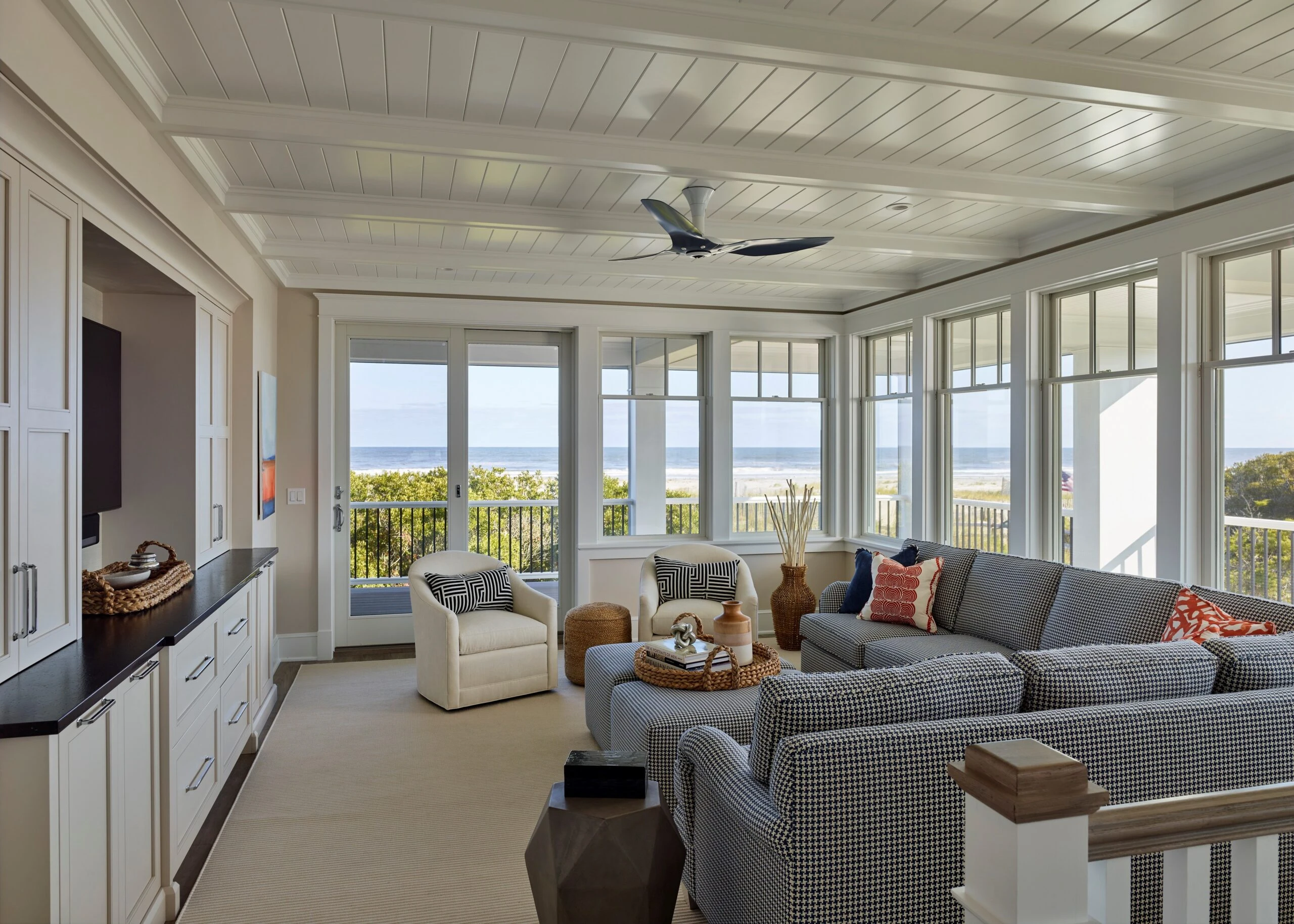 Coastal sunroom with shiplap ceiling, French doors, clerestory windows, checkered sectional sofa, and ocean views.