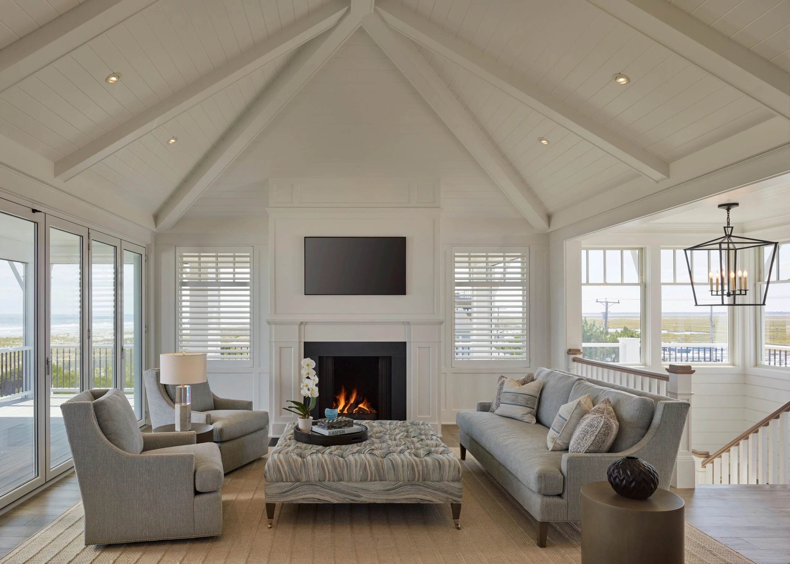 Coastal living room with cathedral ceiling, shiplap walls, fireplace, built-in shelving, and expansive glass doors overlooking water views.