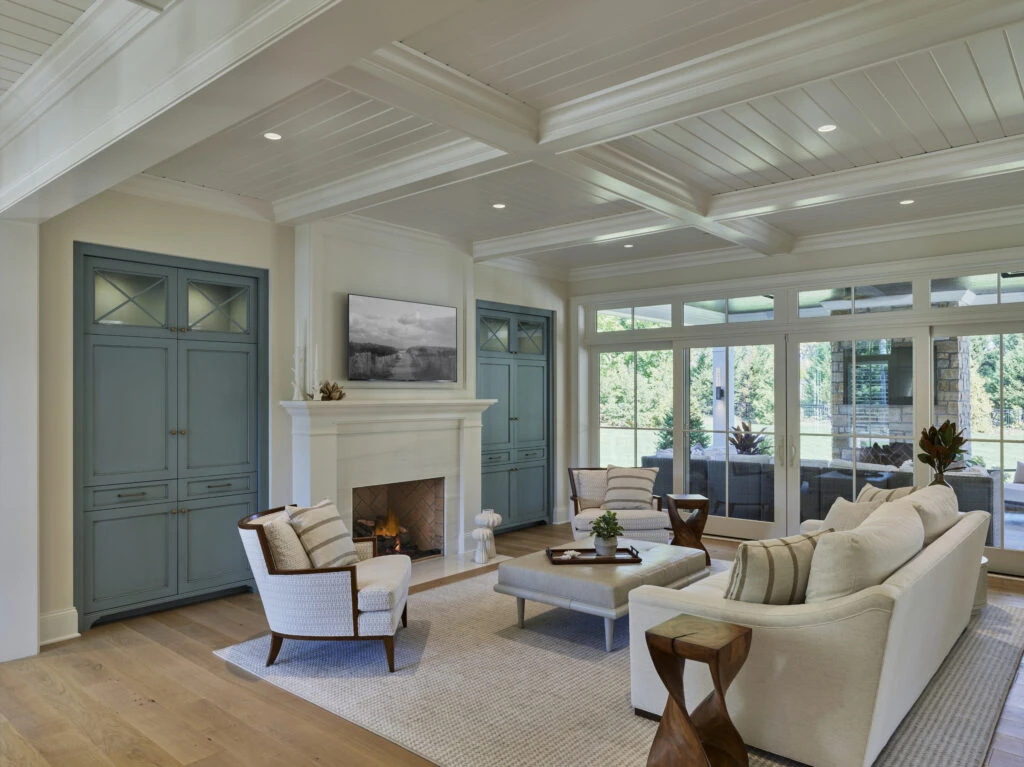 Modern living room with coffered ceiling, fireplace, built-in cabinetry, and expansive glazing overlooking landscape.