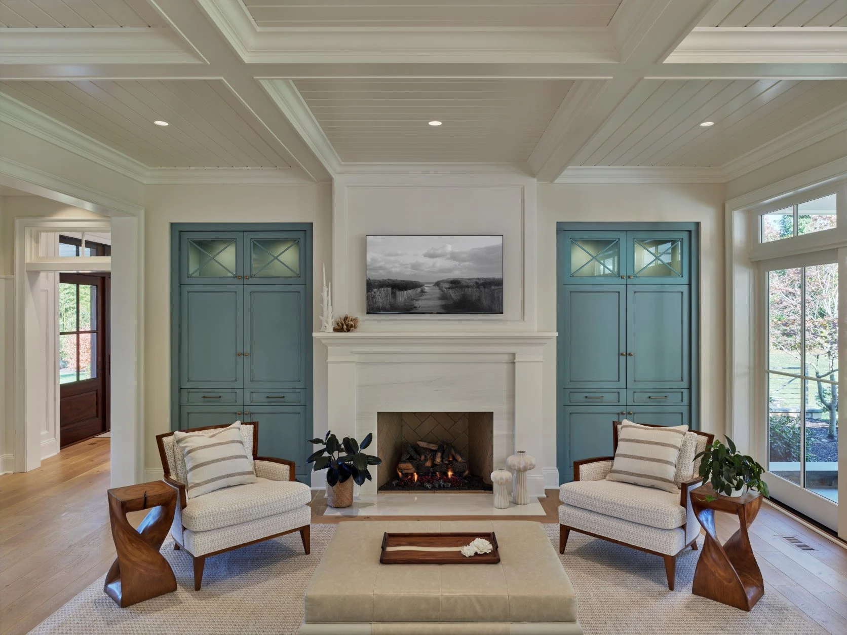 Symmetrical living room with coffered ceiling, fireplace, teal built-in cabinetry, and paired French doors flanking windows.