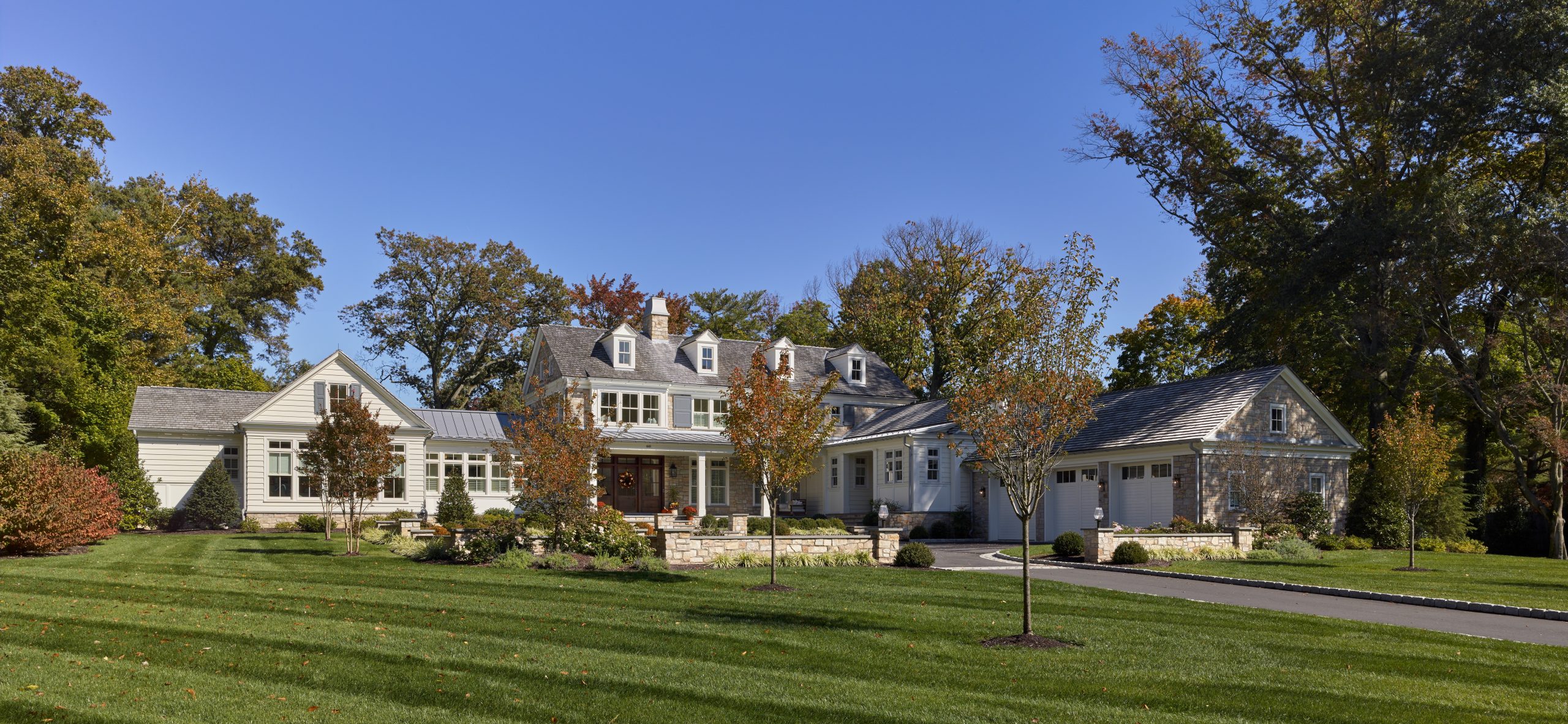 Modern farmhouse estate with white board-and-batten siding, multiple roof lines, and attached garage on manicured grounds.