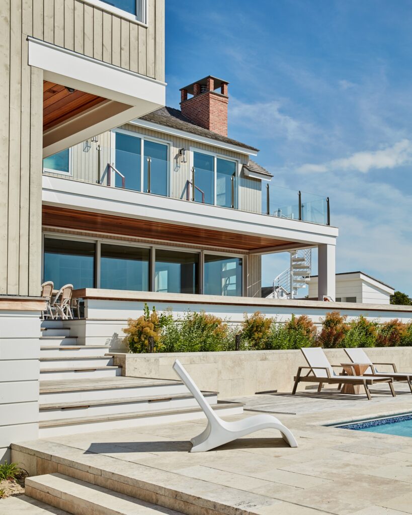Modern waterfront home with horizontal siding, multi-level decking, and extensive glazing overlooking pool and landscape.