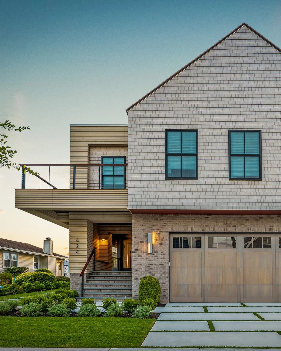 Modern residential home with mixed-material facade combining cedar siding, brick, and shingle cladding with cantilevered deck and metal railing.