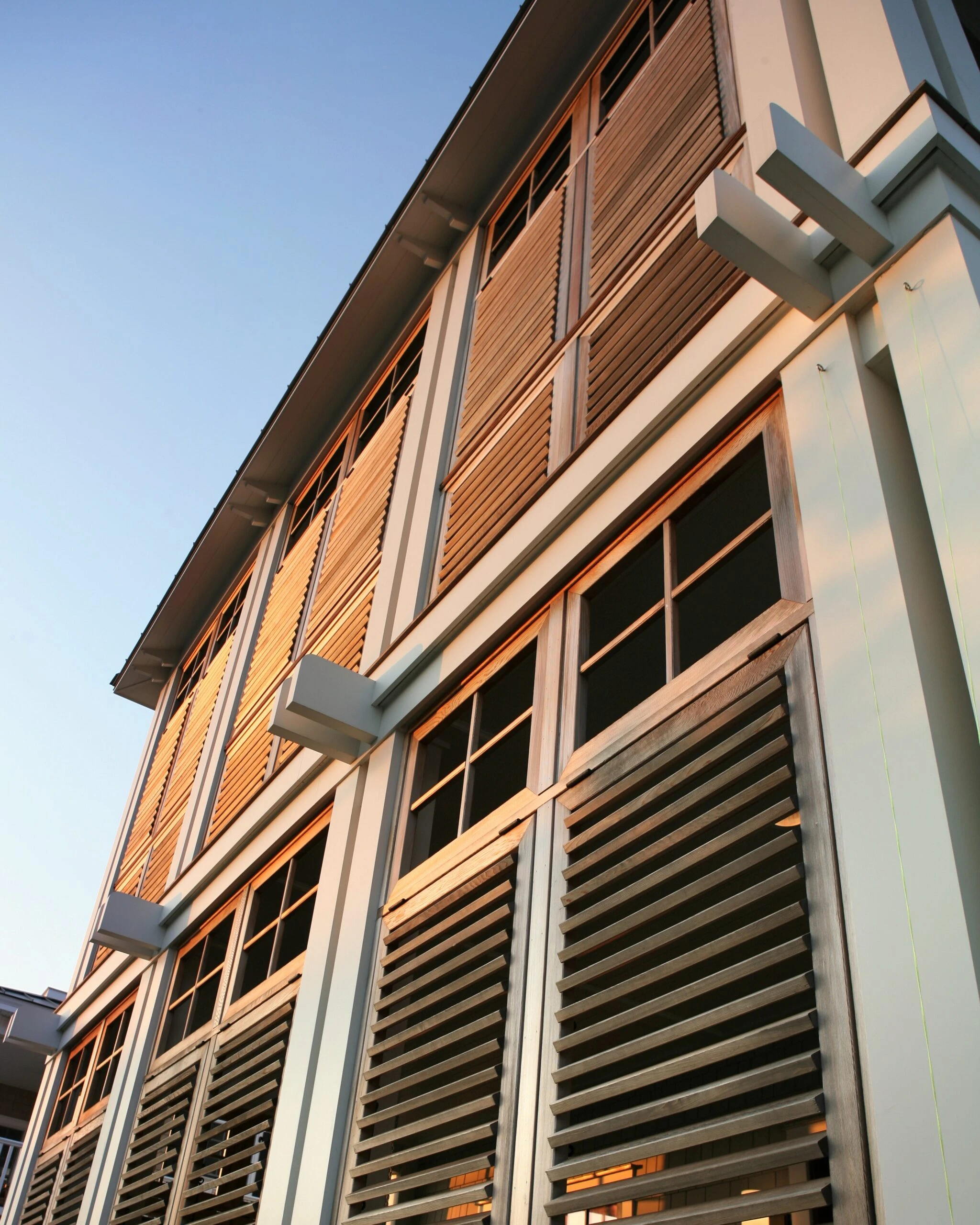 Modern building facade featuring horizontal wood siding, metal framing, and louvered window screens in warm tones.