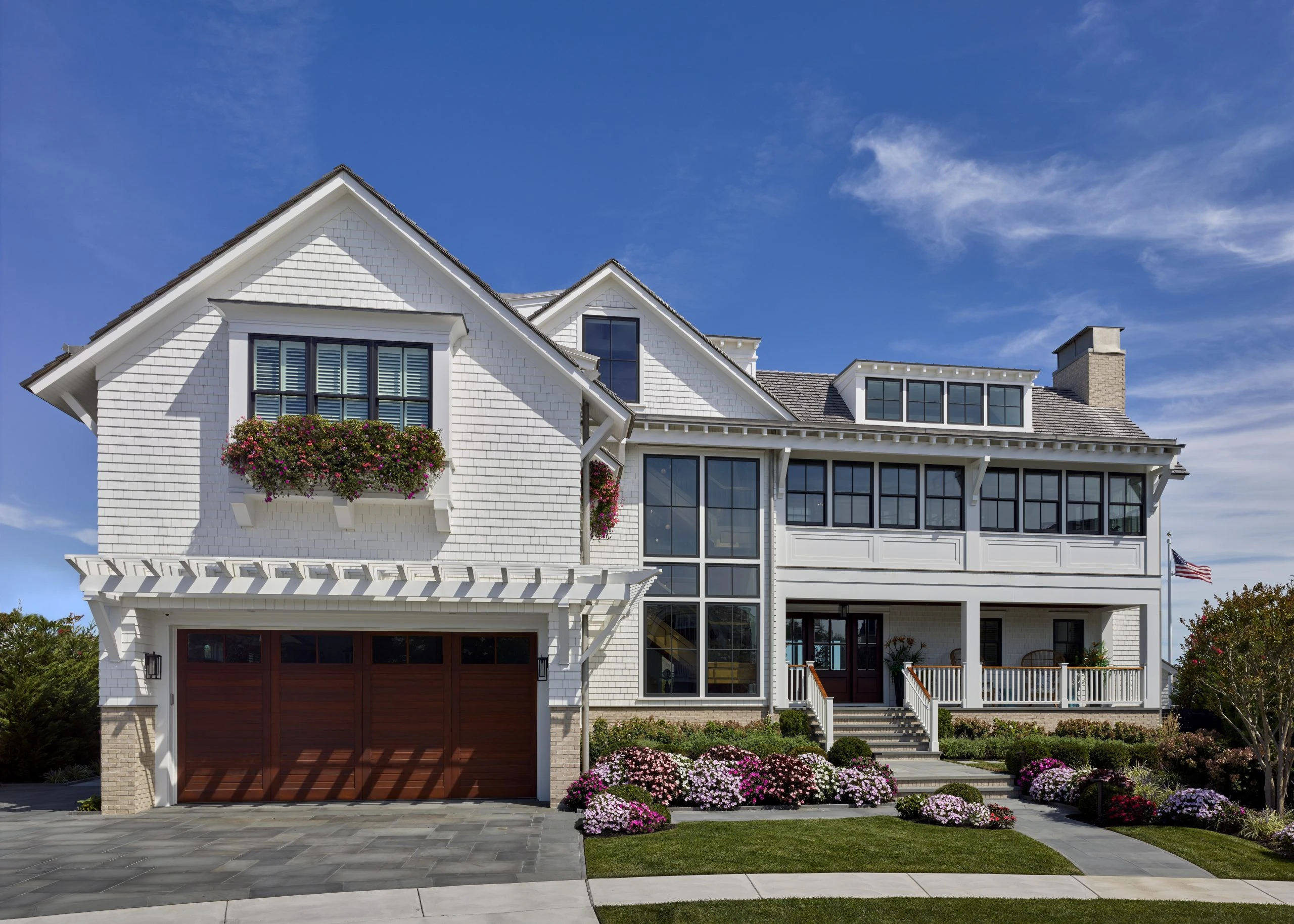 Contemporary coastal home with white shingle facade, gabled roofline, dark wood garage door, and multi-pane windows.
