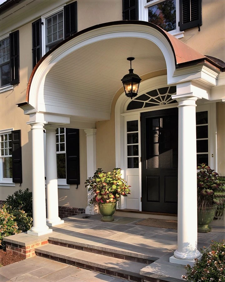 Residential entry portico with curved barrel vault, white columns, black double doors, and brick facade.
