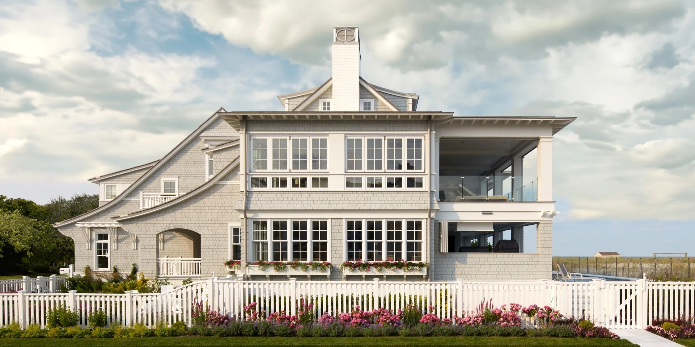 Modern shingle-style coastal house with clean lines, expansive multi-pane windows, and a central cupola.