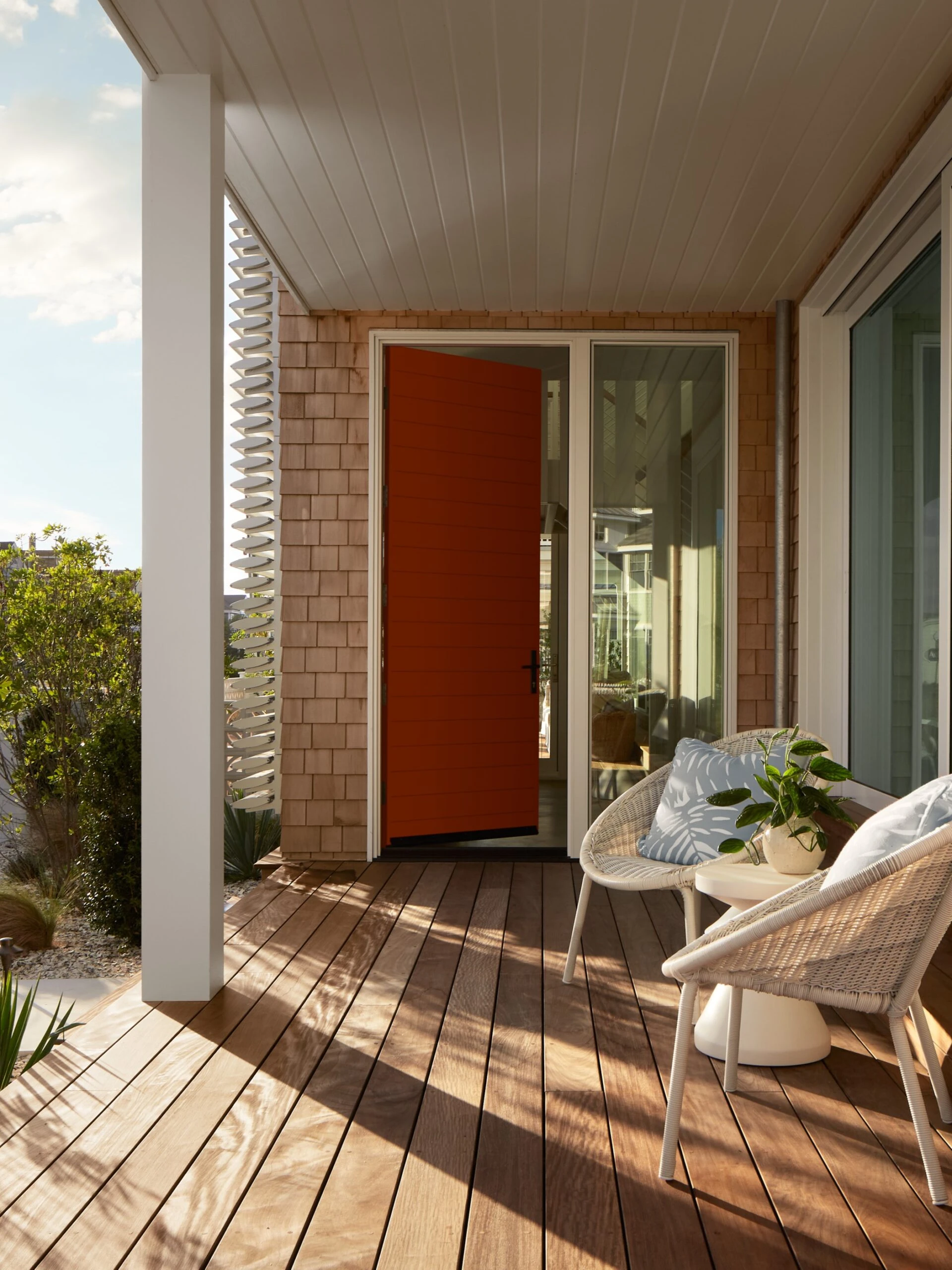Modern residential deck with composite decking, white ceiling soffit, brick chimney, red entry door, and contemporary wicker seating.