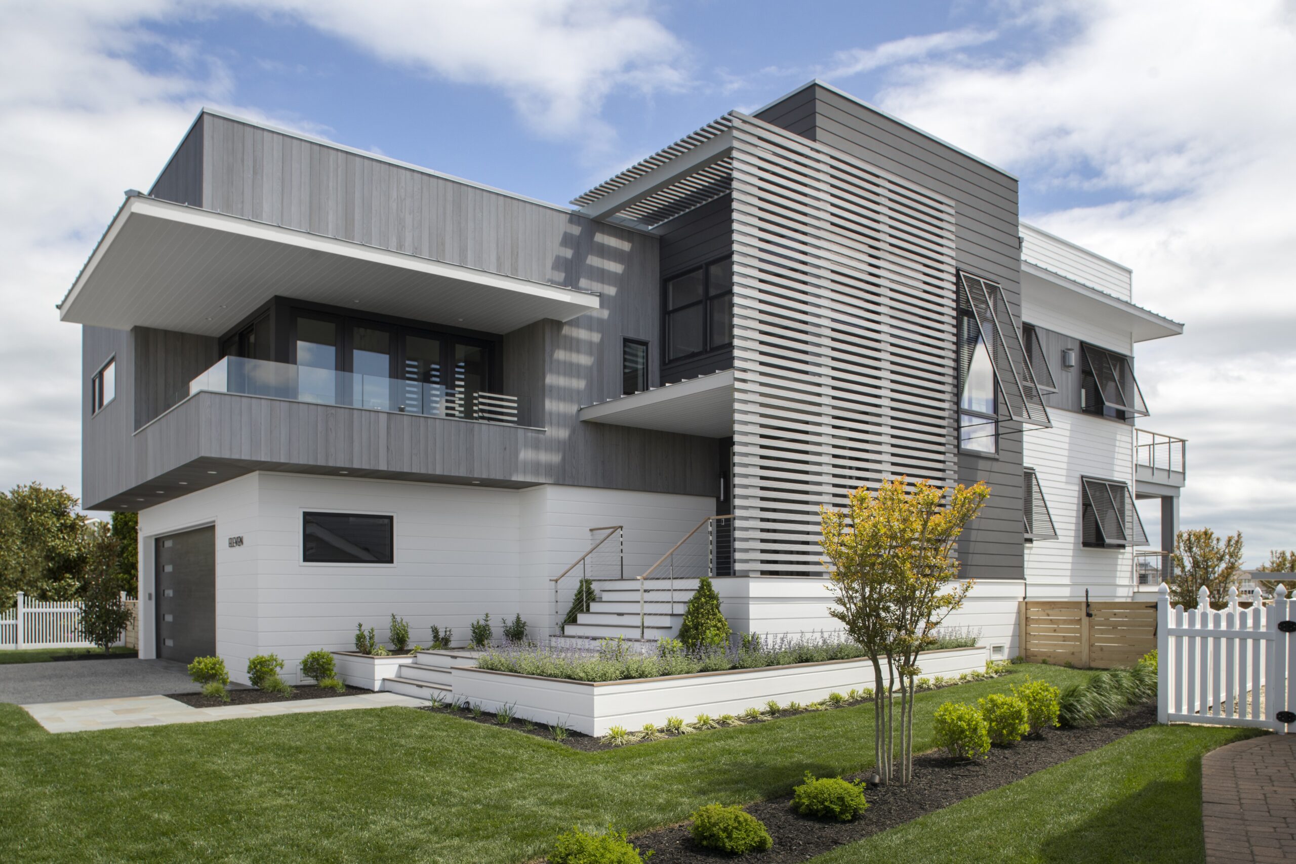Modern two-story residential home with horizontal metal siding, white base, cantilevered balcony, and louvered sun shades.