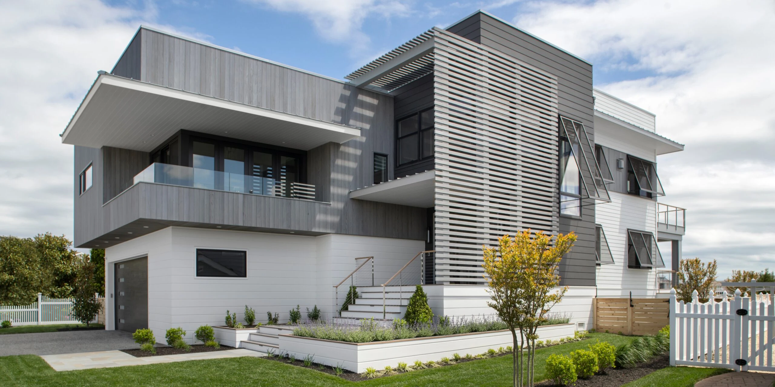 Modern two-story residential home with mixed metal and white cladding, cantilevered upper level, and horizontal louver detailing.