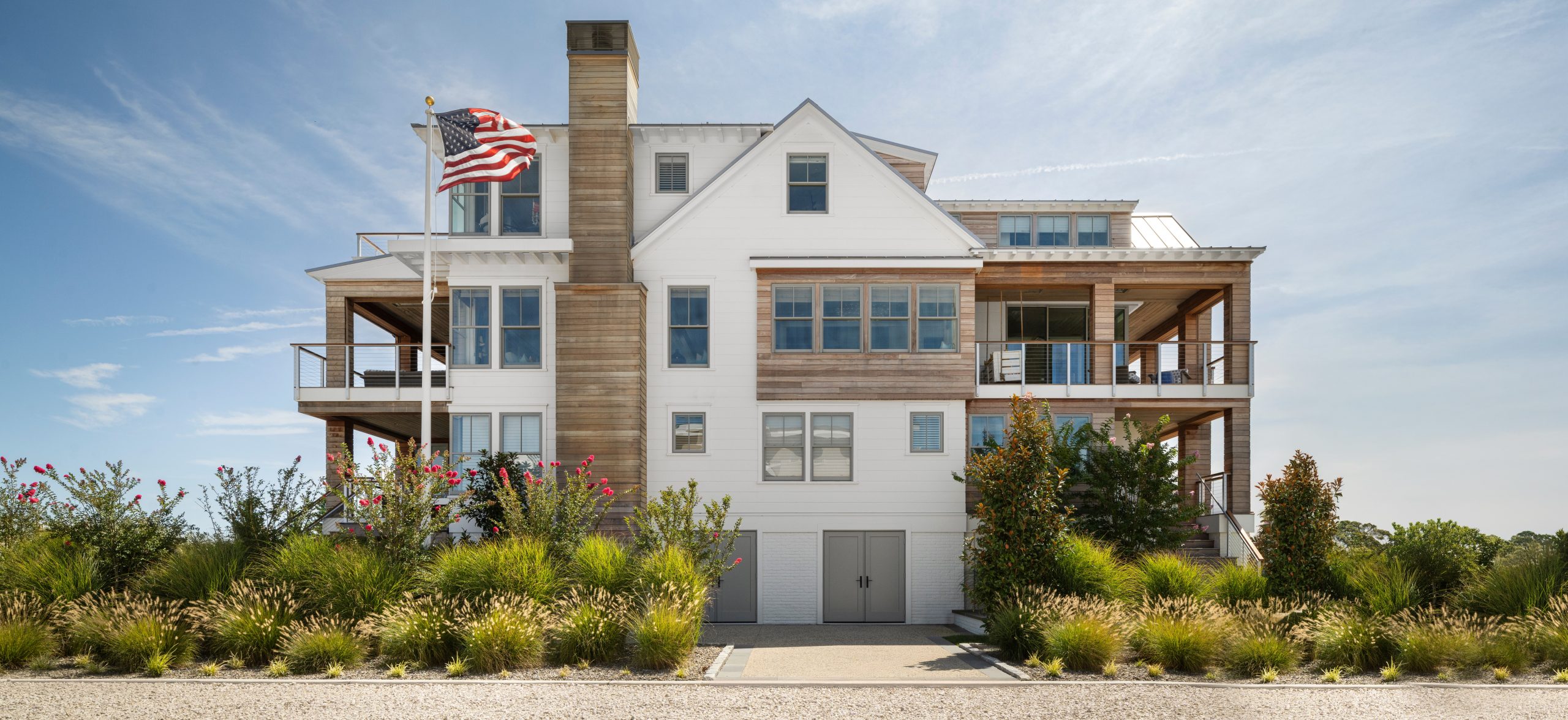 Modern coastal residence with mixed material facade, elevated design, continuous decking, and central chimney stack.