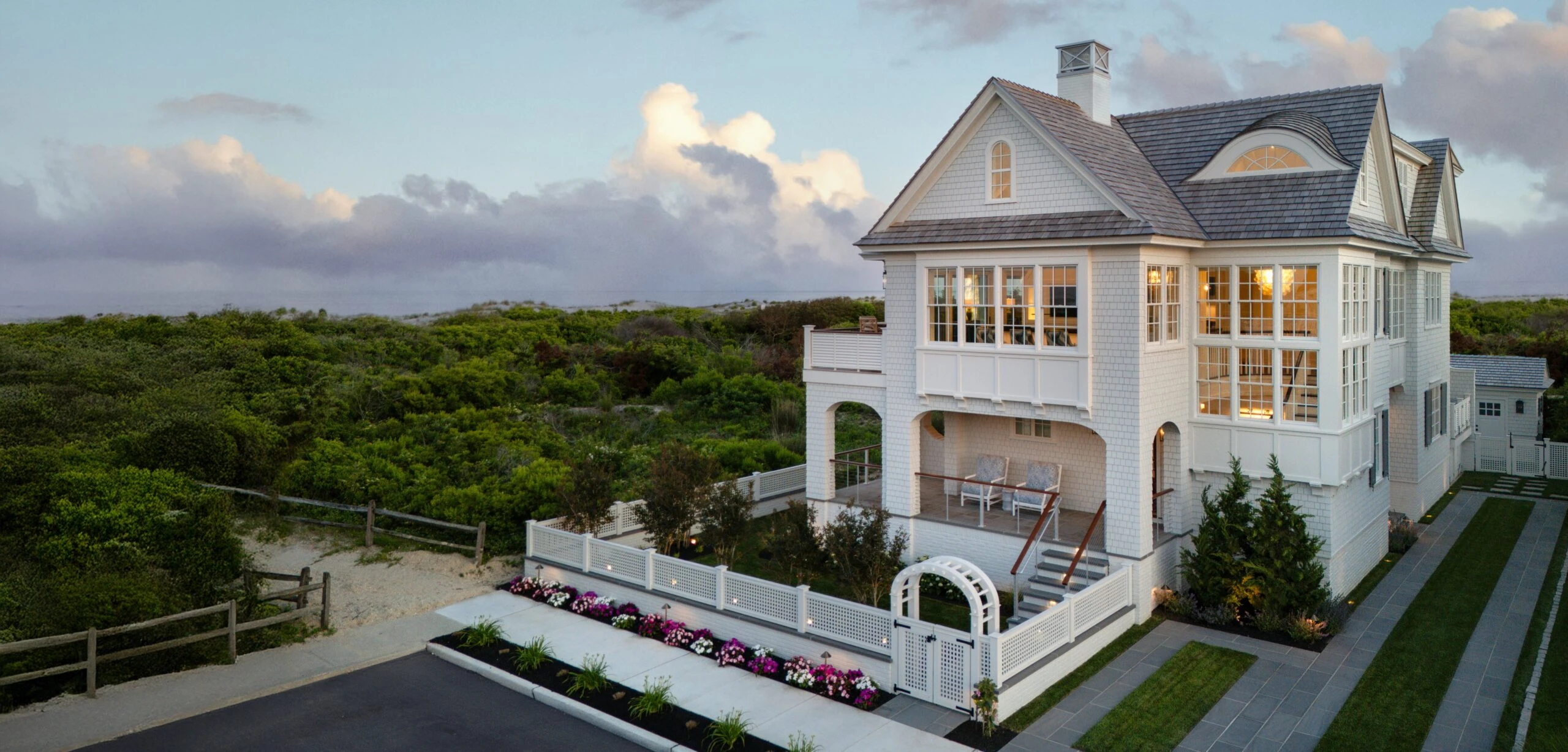 Modern coastal residence with white shingle facade, multiple gables, and extensive glazing overlooking landscaped grounds.