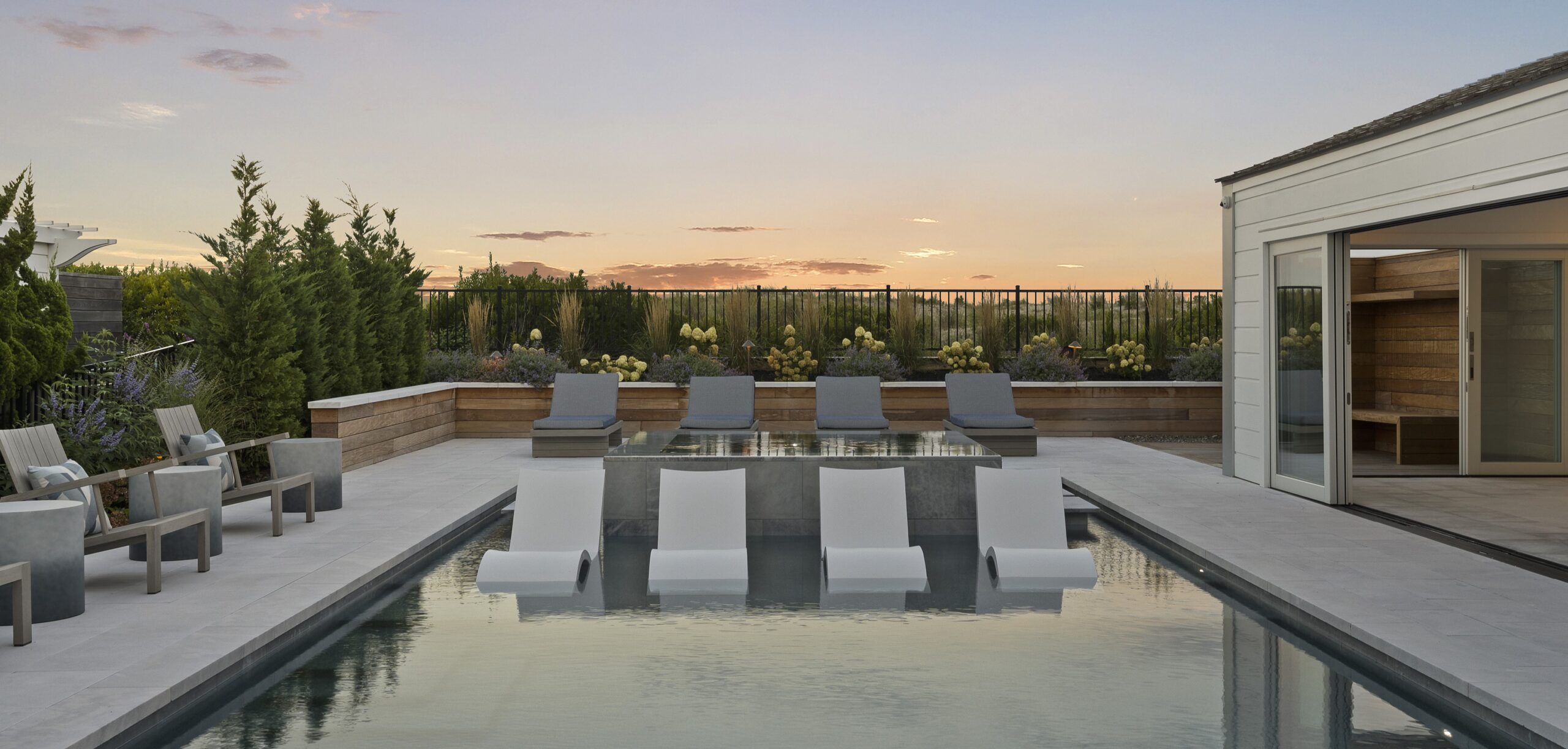 Modern rooftop terrace with linear pool, concrete loungers, and minimalist seating overlooking manicured landscape and city skyline.