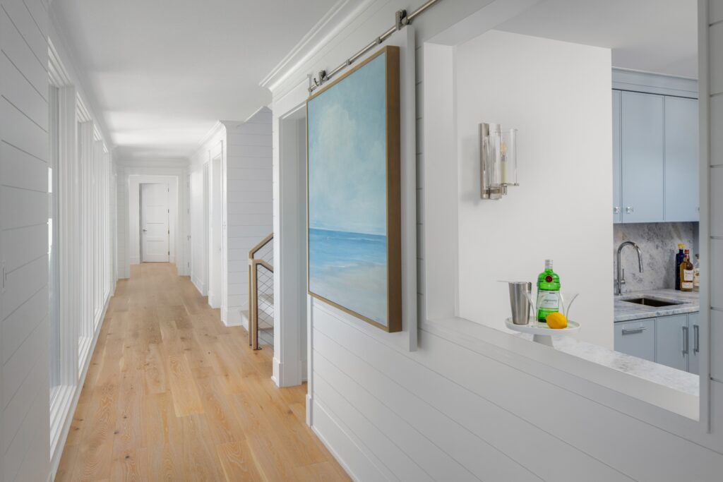 Modern hallway with shiplap walls, wood flooring, built-in shelving, and coastal artwork framed in sliding barn door style.